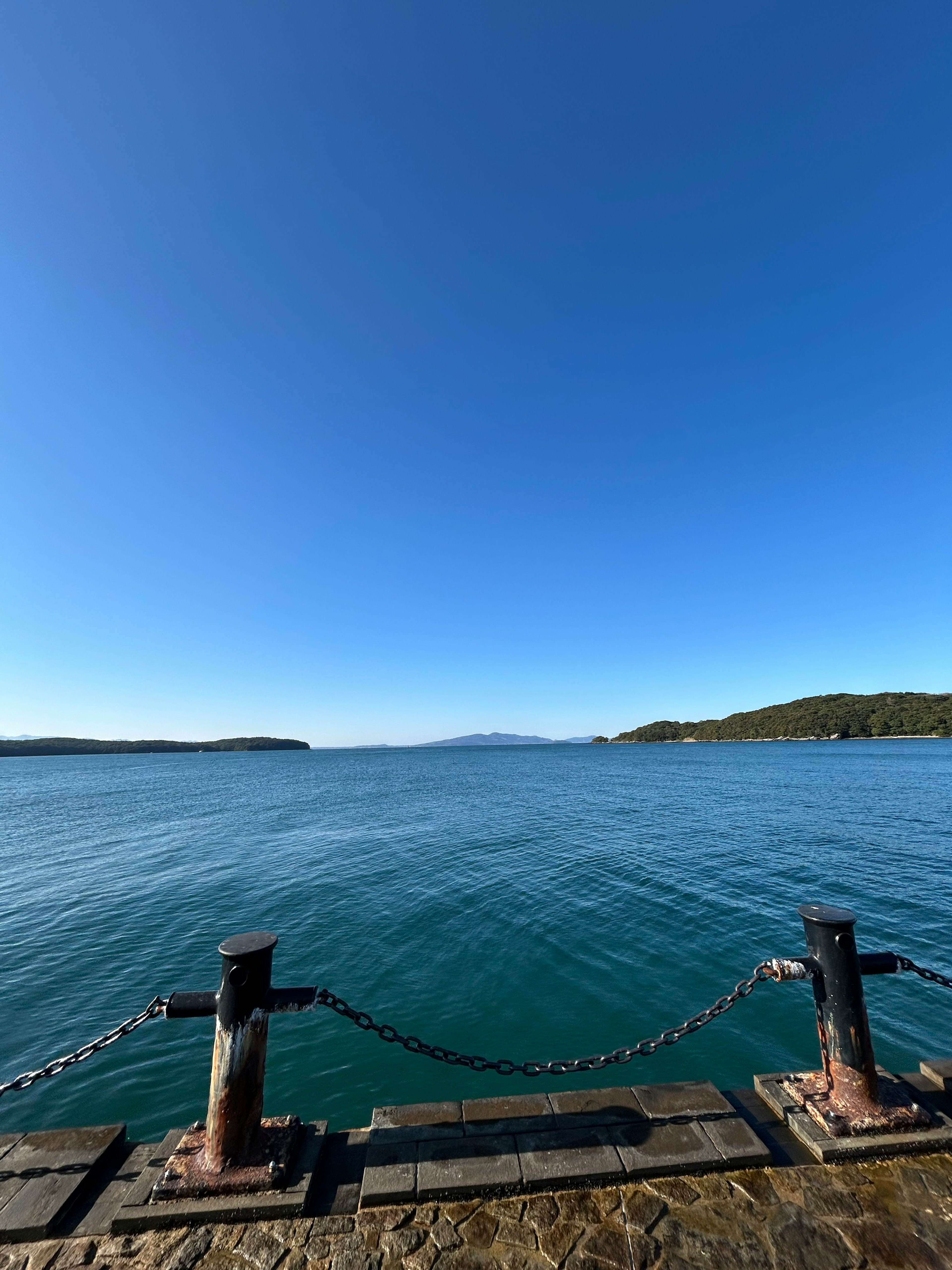 Scenic view of blue water and clear sky with a quiet pier and chain