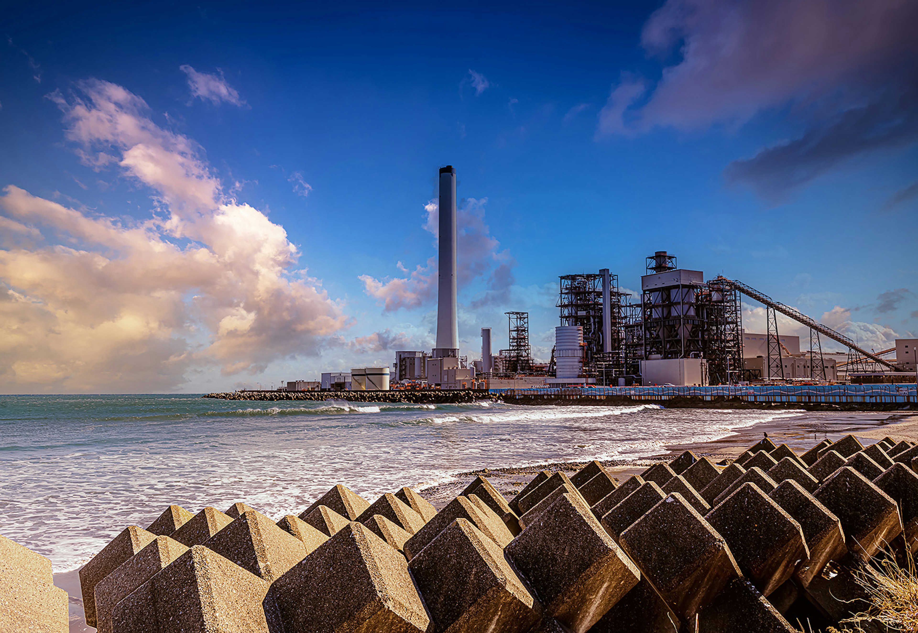 Coastal industrial landscape featuring a tall smokestack and factory buildings