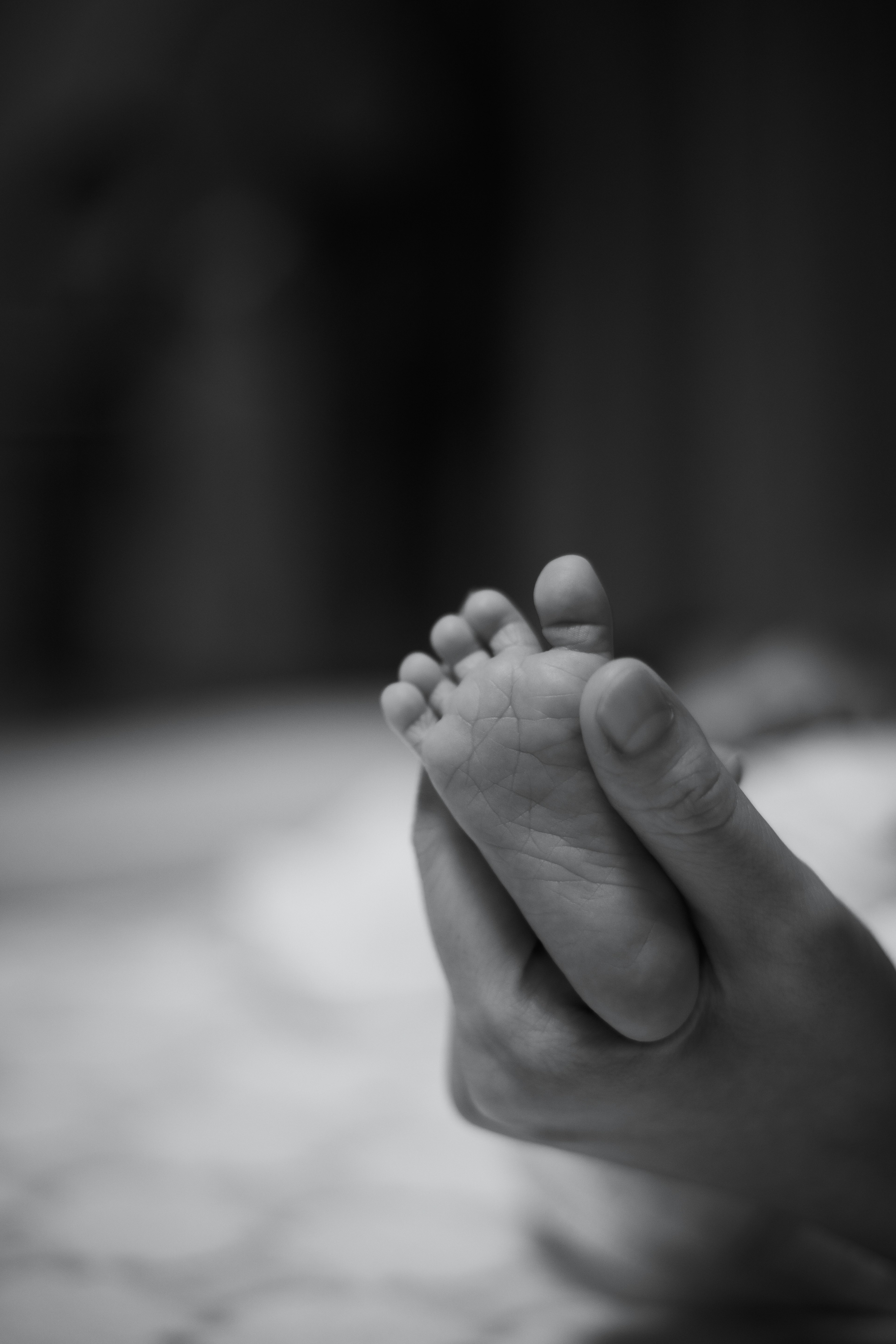 A monochrome image of a hand gently holding a baby's foot