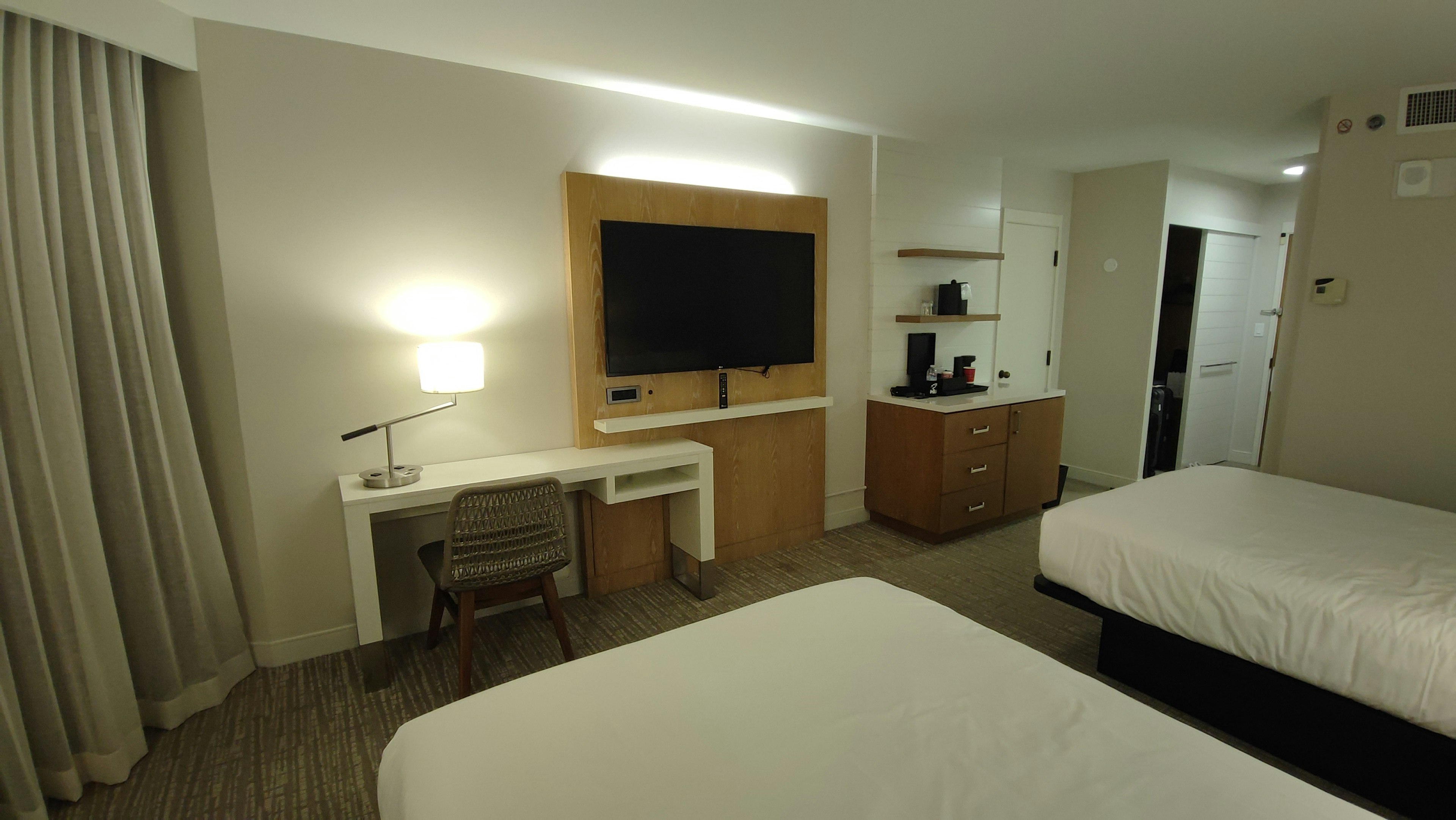 Modern hotel room featuring two beds, a television, a desk, and a coffee maker