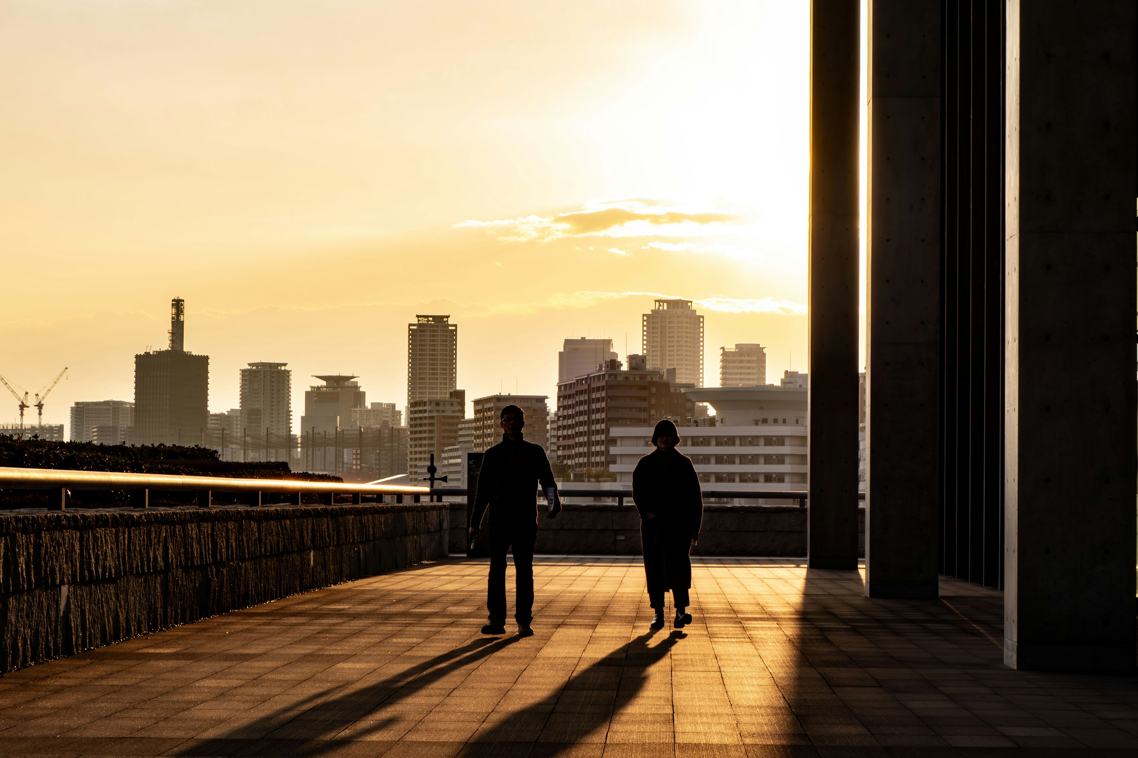 Due figure che camminano contro un tramonto con skyline urbano