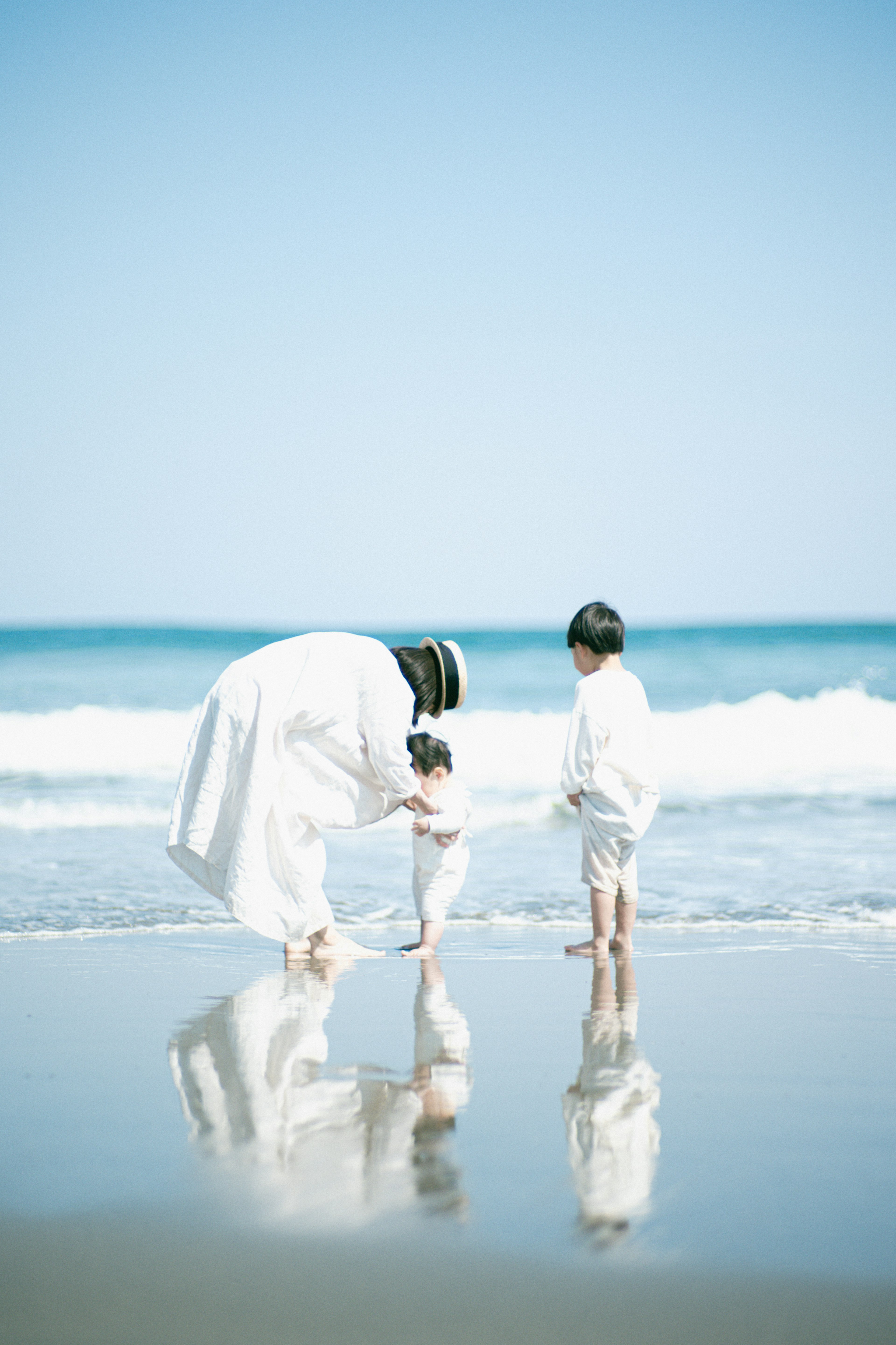 Children playing at the beach with an adult Blue sky and wave reflections create a serene atmosphere