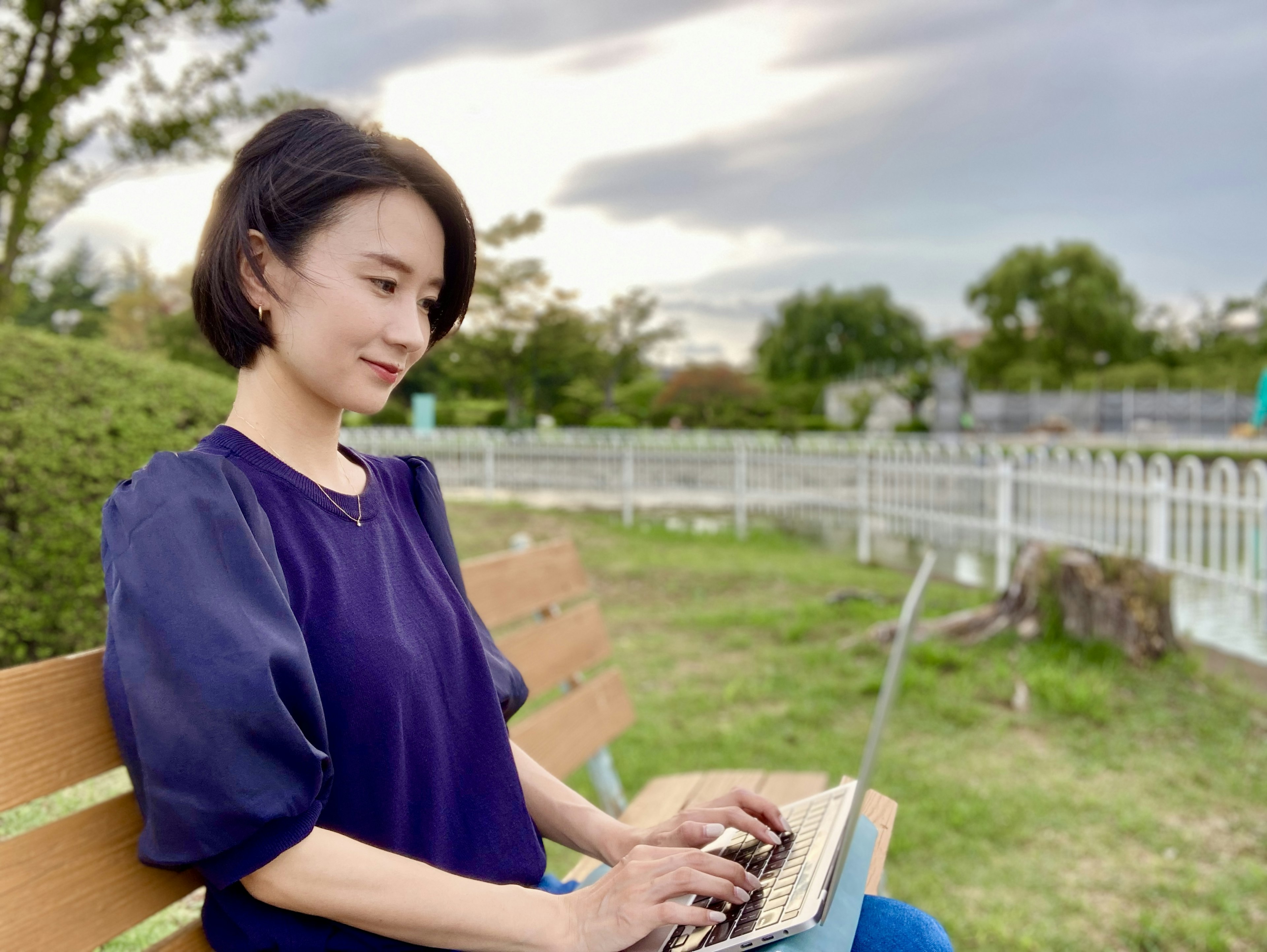 Frau, die an einem Laptop arbeitet, während sie auf einer Bank in einem Park sitzt