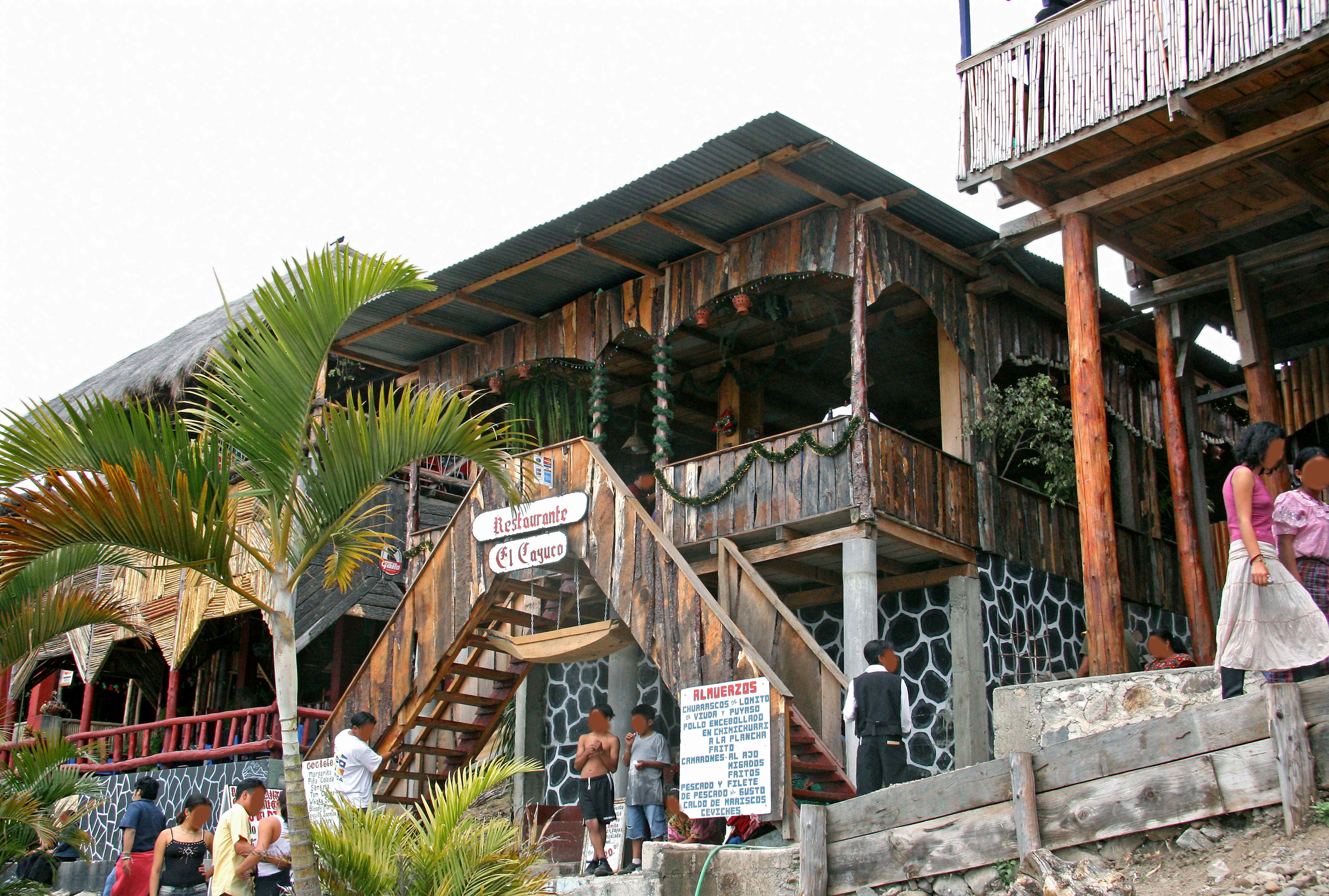 Edificio de restaurante de madera con escaleras y palmeras visibles