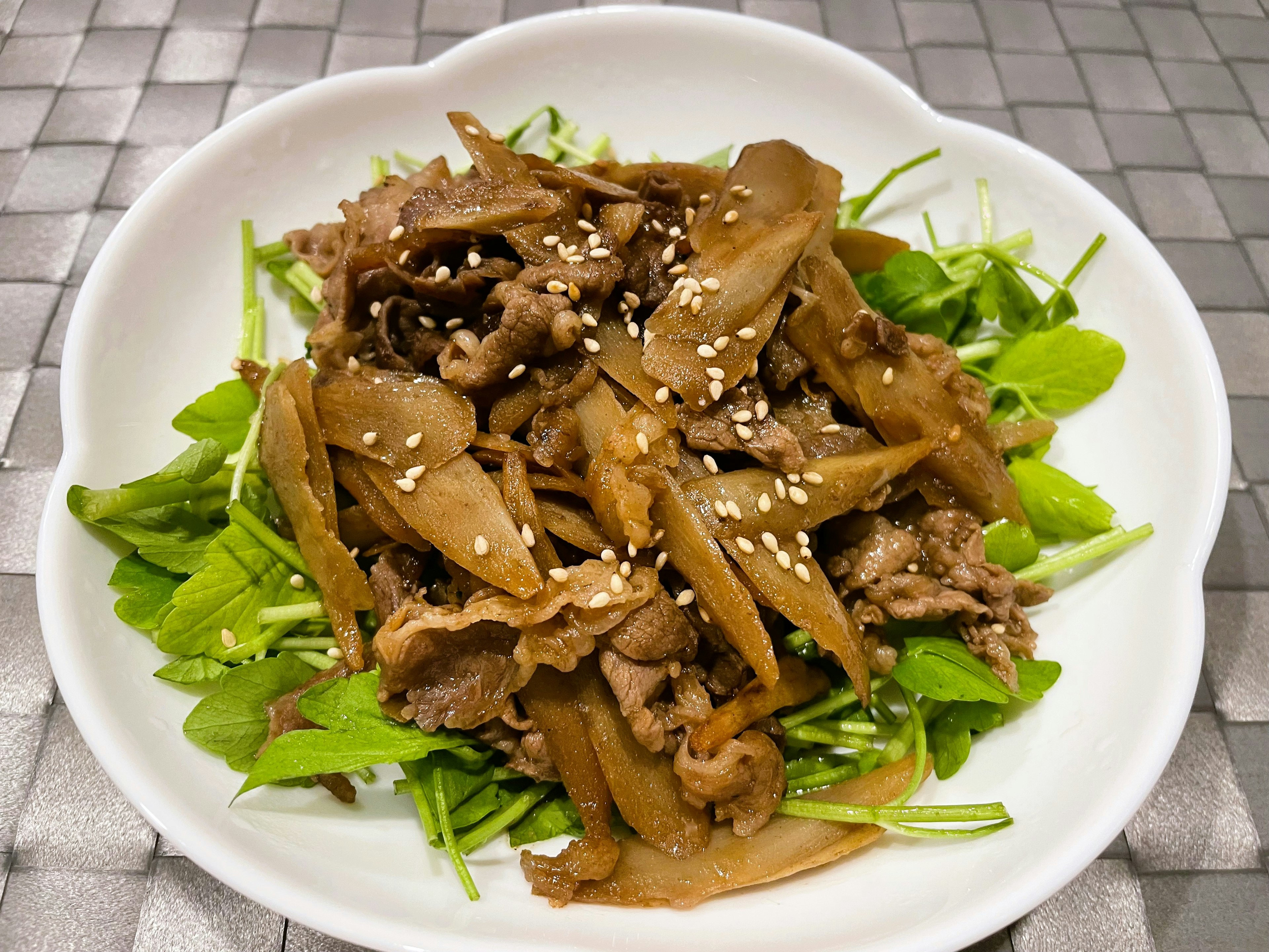 Une salade de viande et de légumes servie dans une assiette blanche avec des graines de sésame