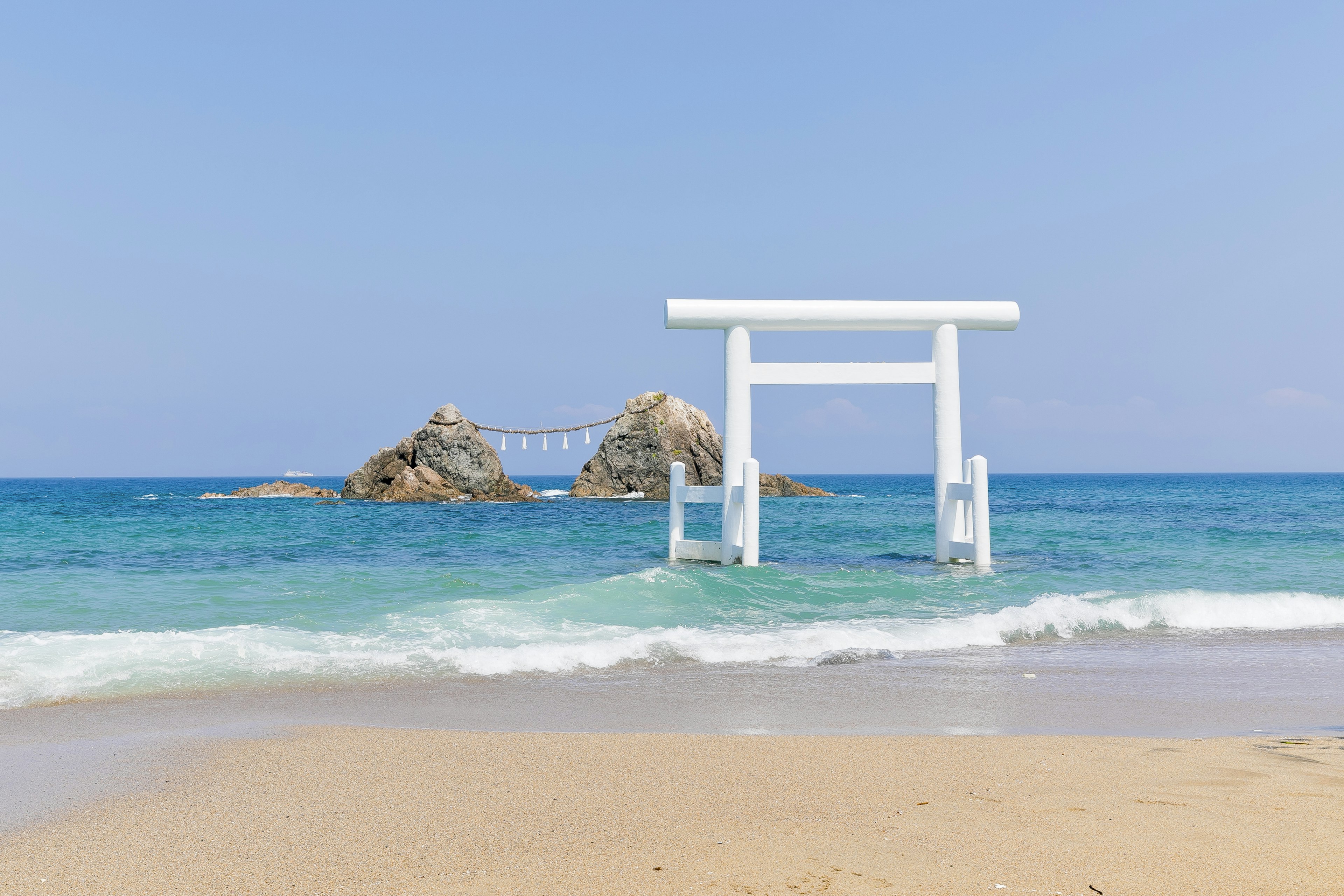 A white torii gate stands in the ocean at a beautiful beach