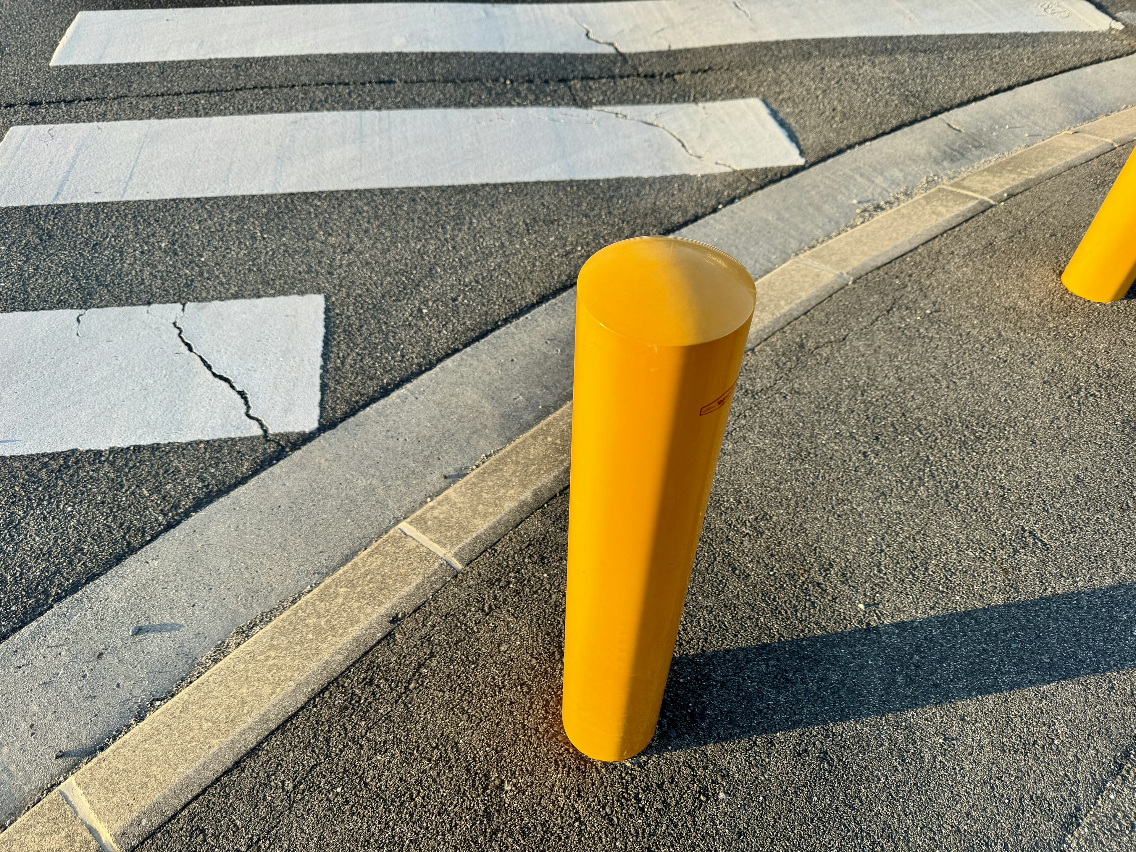 A yellow bollard near a pedestrian crosswalk on pavement