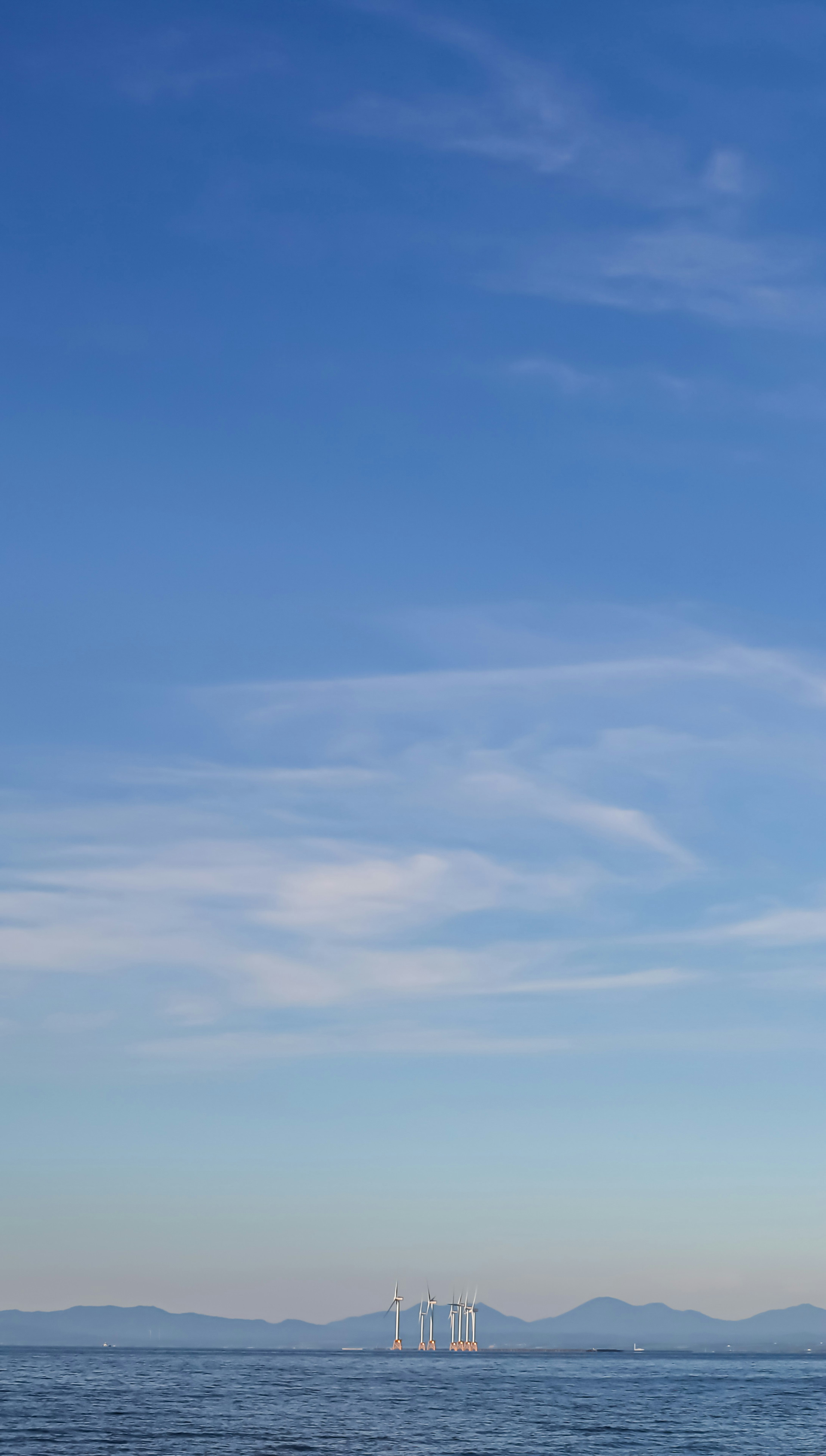 Un paysage serein avec un ciel bleu et une mer calme avec des silhouettes de montagnes au loin