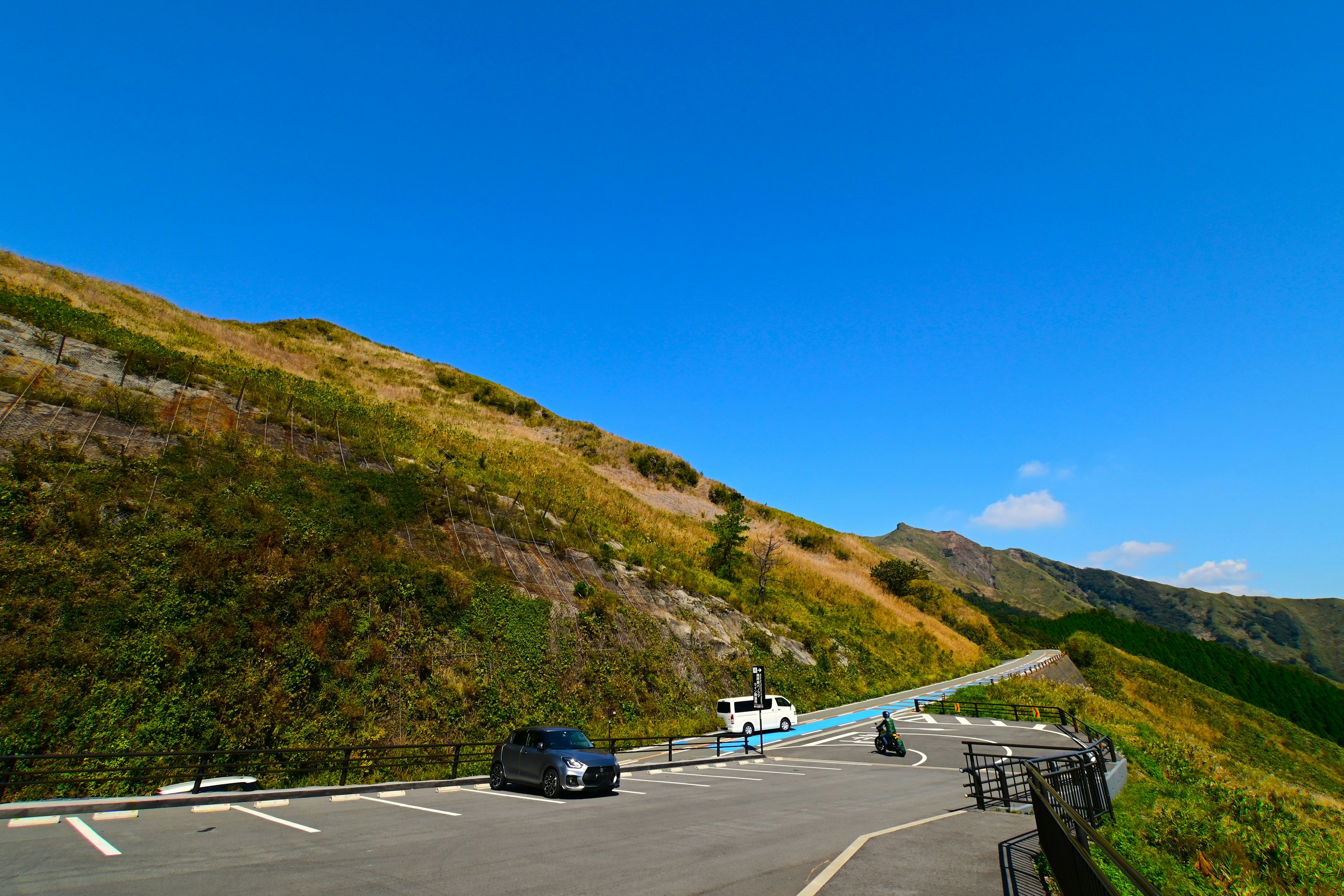 青空の下の山道に沿った車とバイクの風景