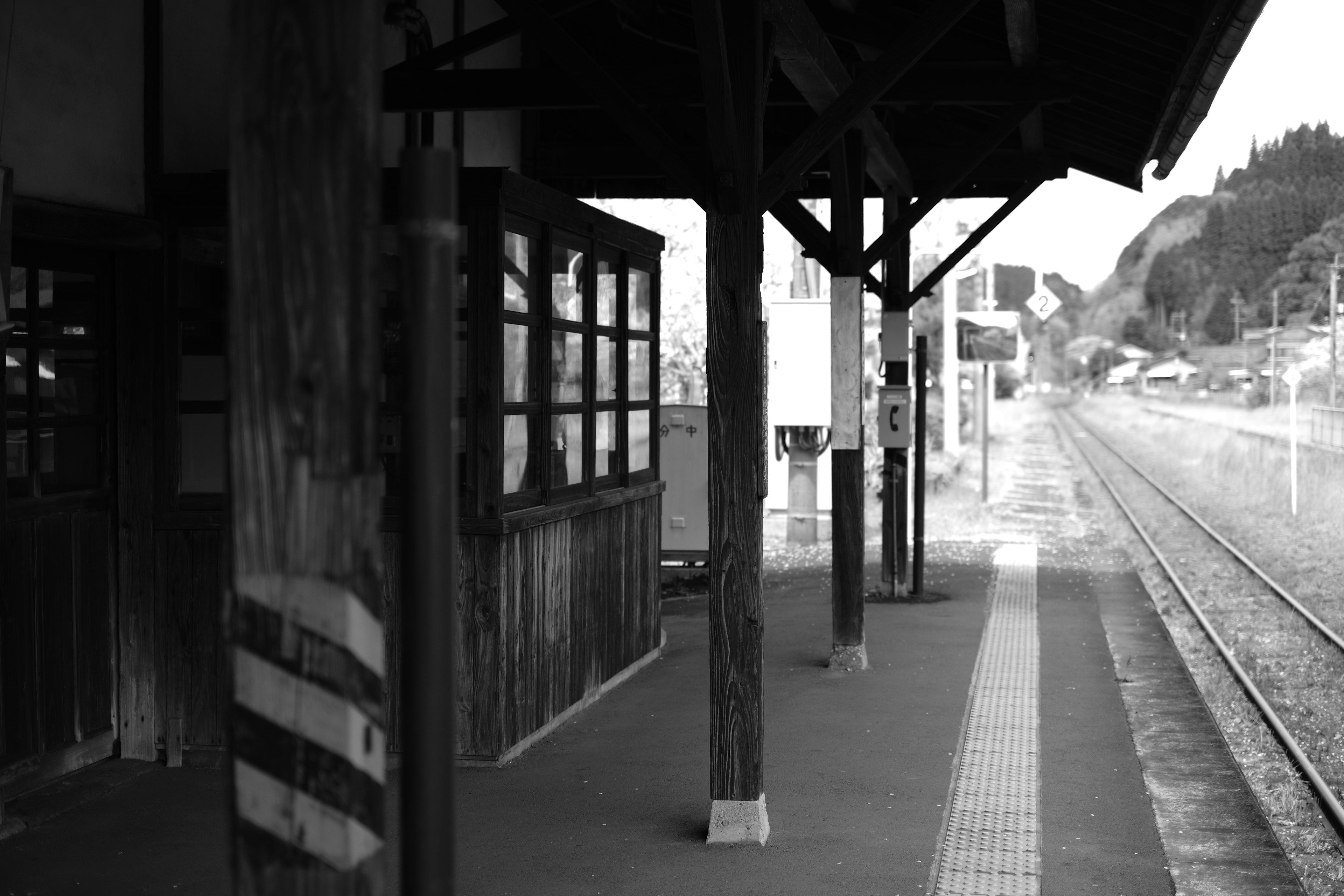 ภาพมุมมองสถานีรถไฟขาวดำ มีเสาไม้และรางรถไฟ