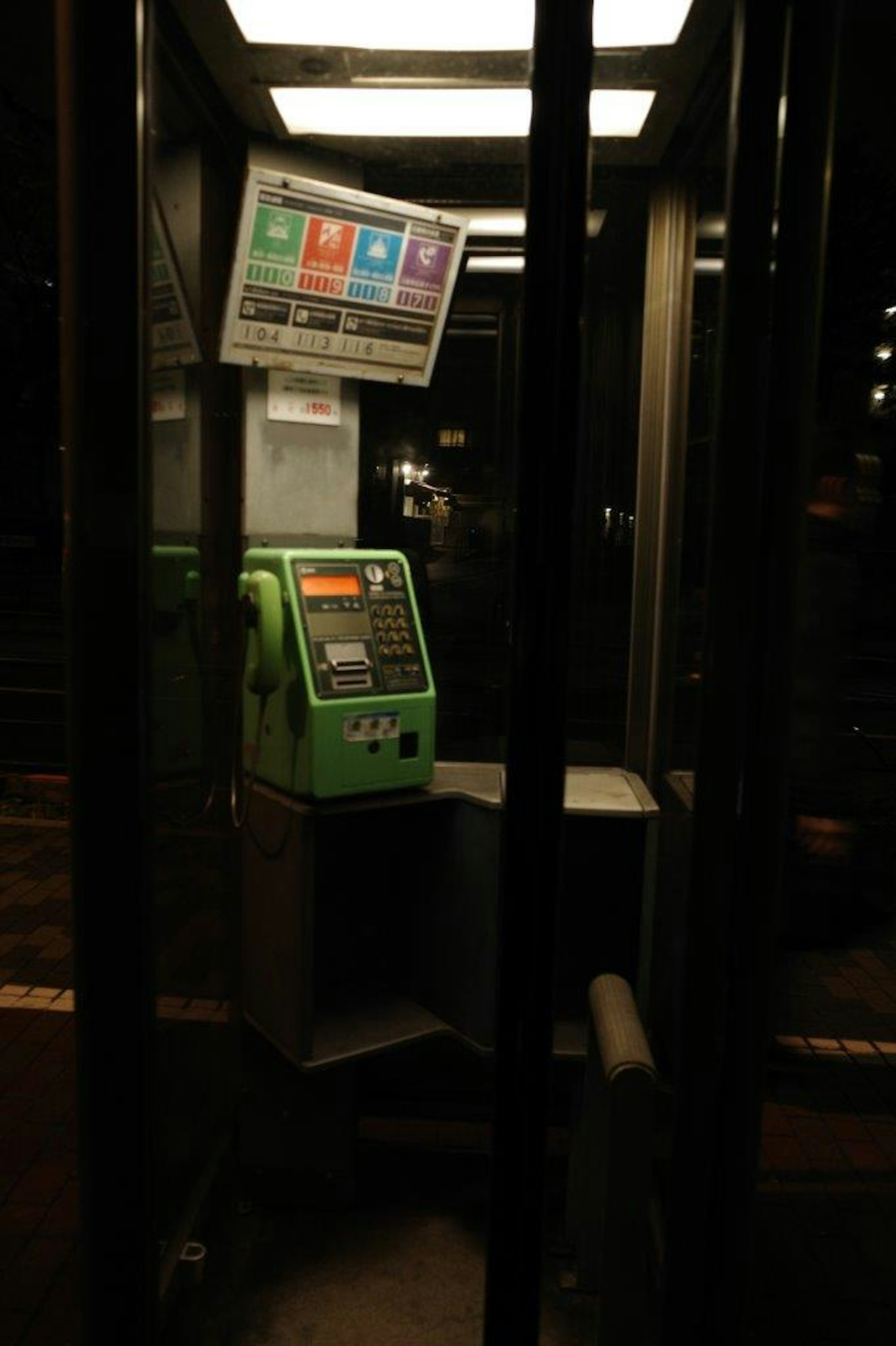 Interior de una cabina telefónica con un teléfono público verde y un cartel informativo