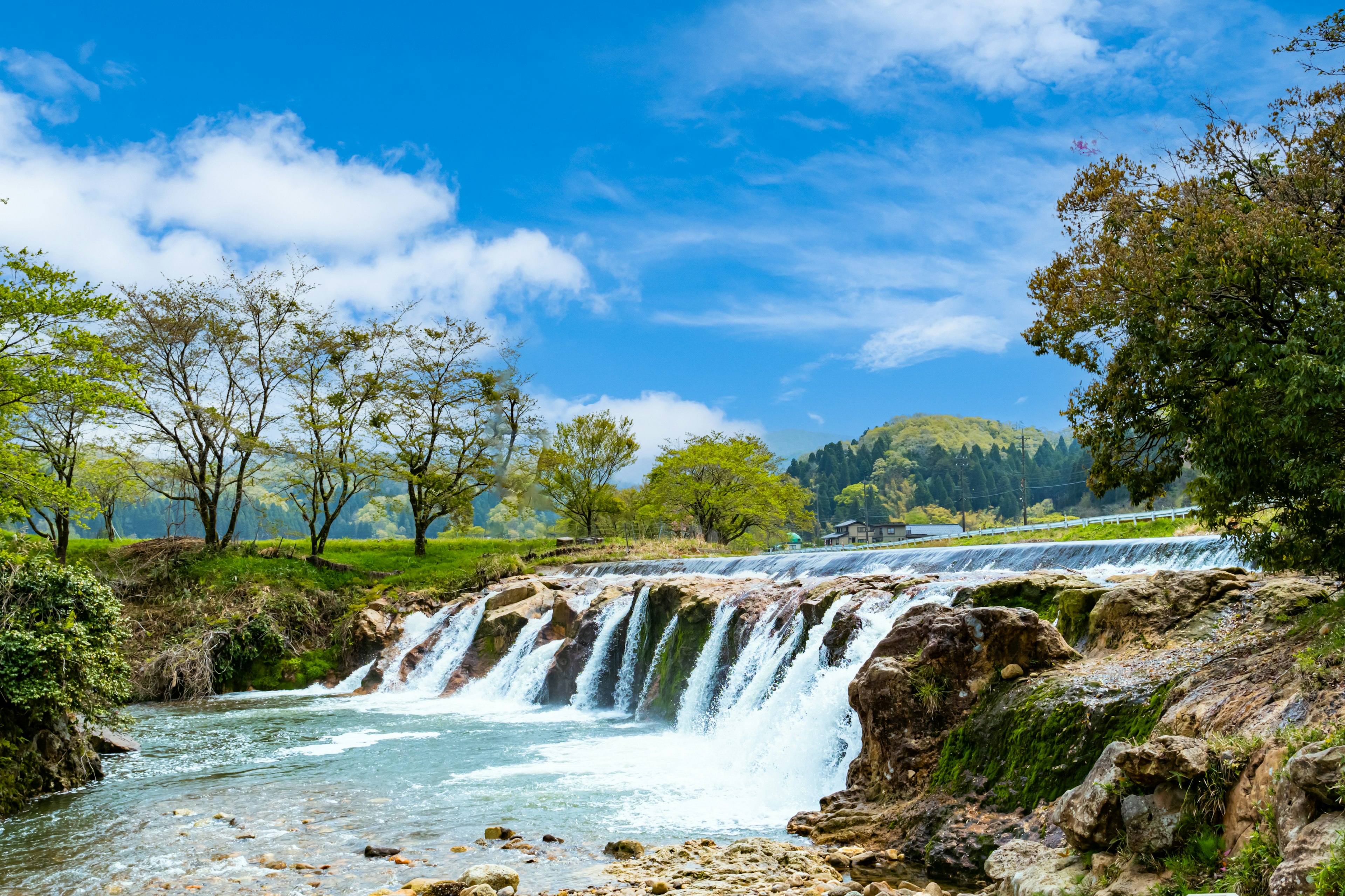 Sebuah air terjun kecil dikelilingi oleh vegetasi subur di bawah langit biru