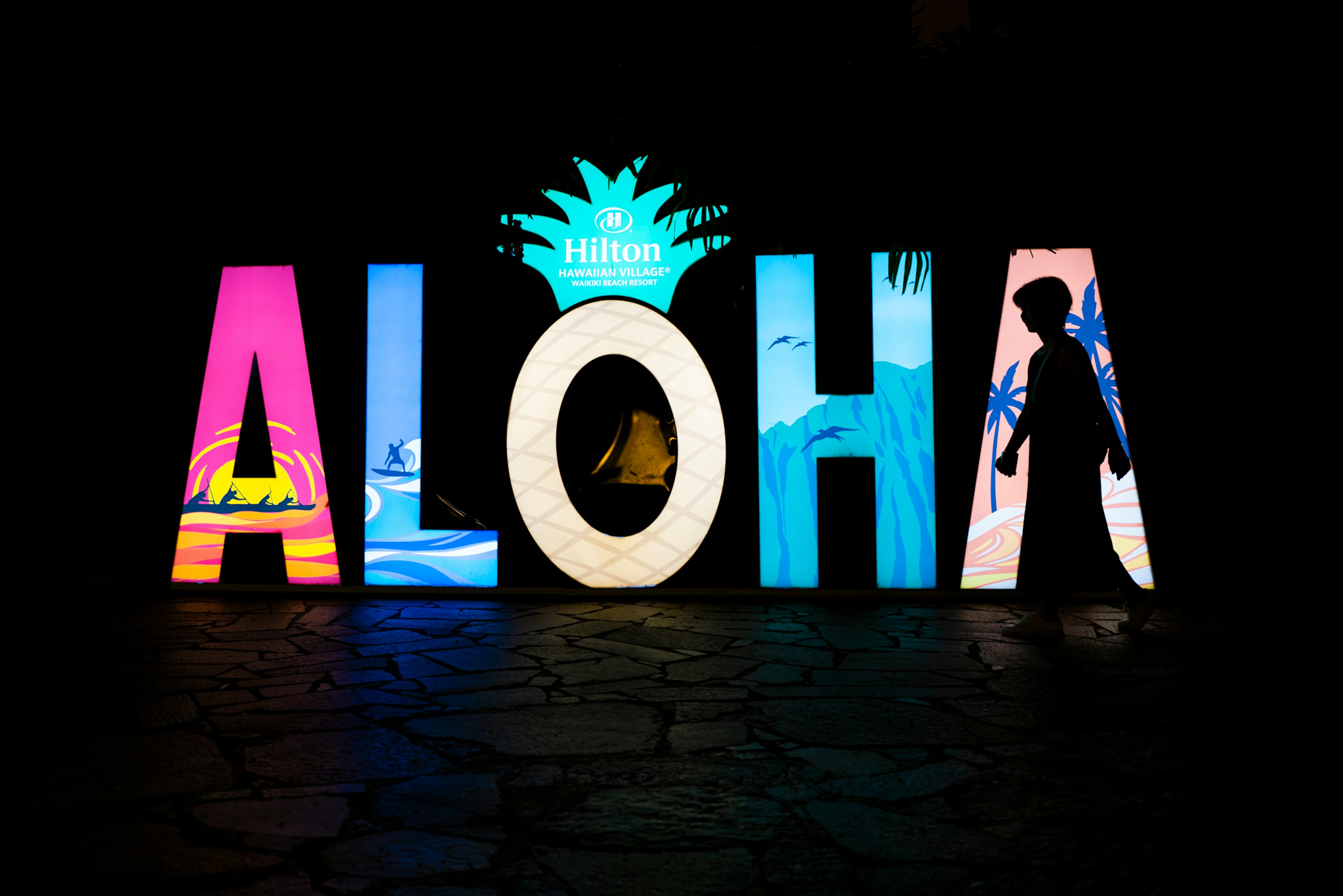 Colorful 'Aloha' sign with vibrant designs set against a dark background