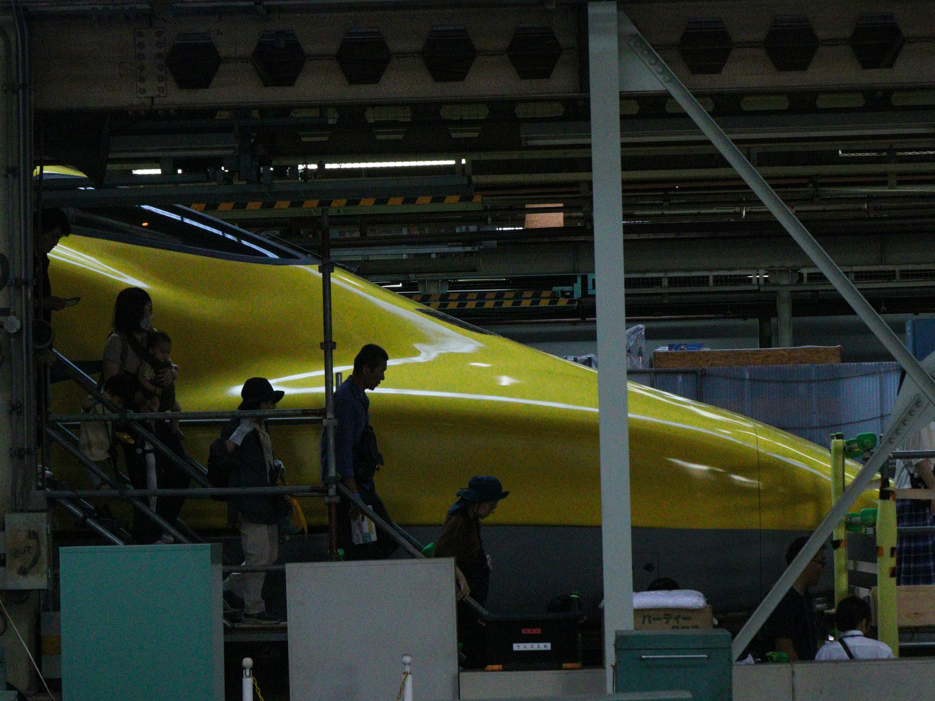 Sección frontal de un Shinkansen amarillo con trabajadores dentro de una fábrica