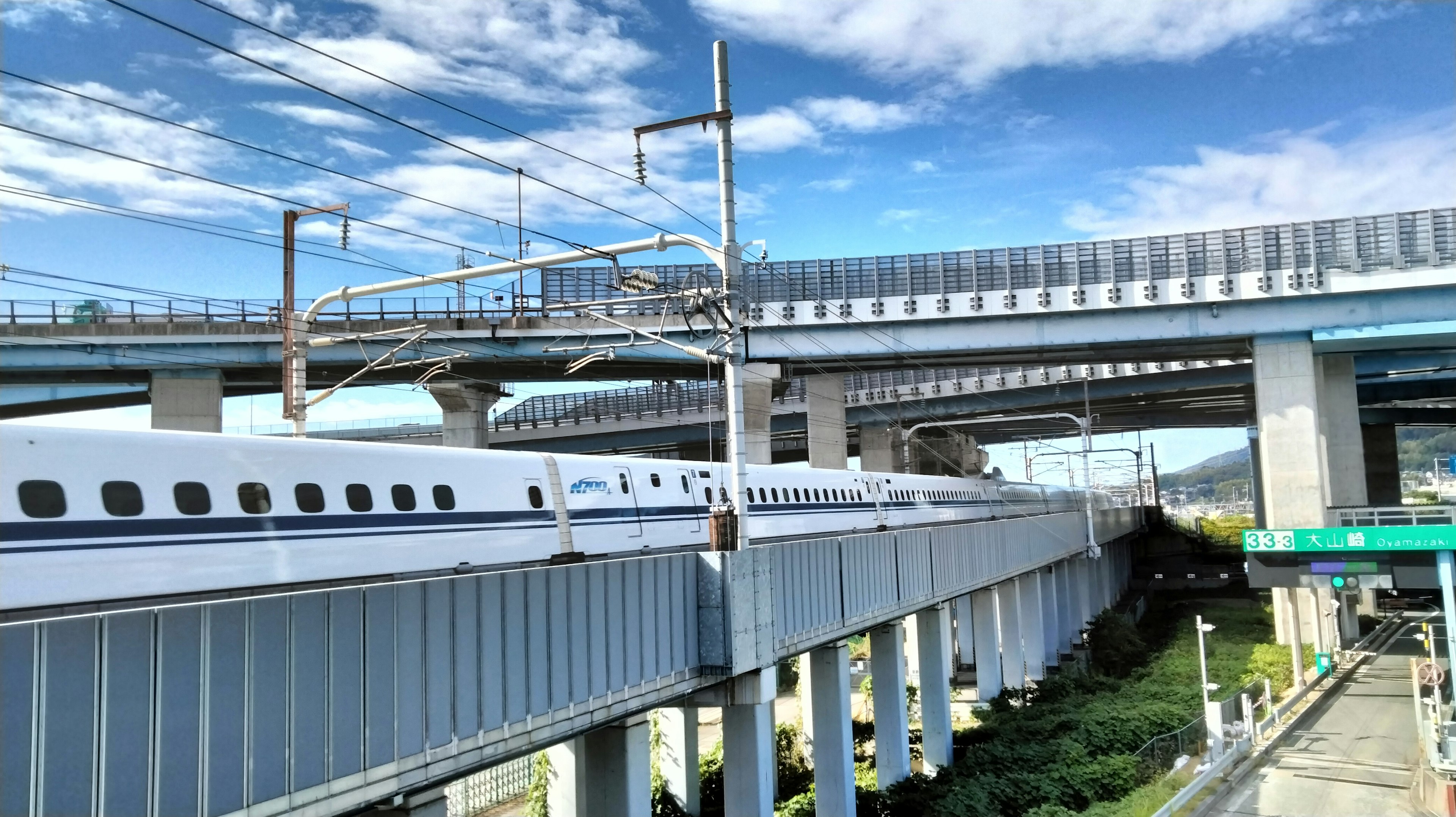 Shinkansen train passing under a highway with blue sky