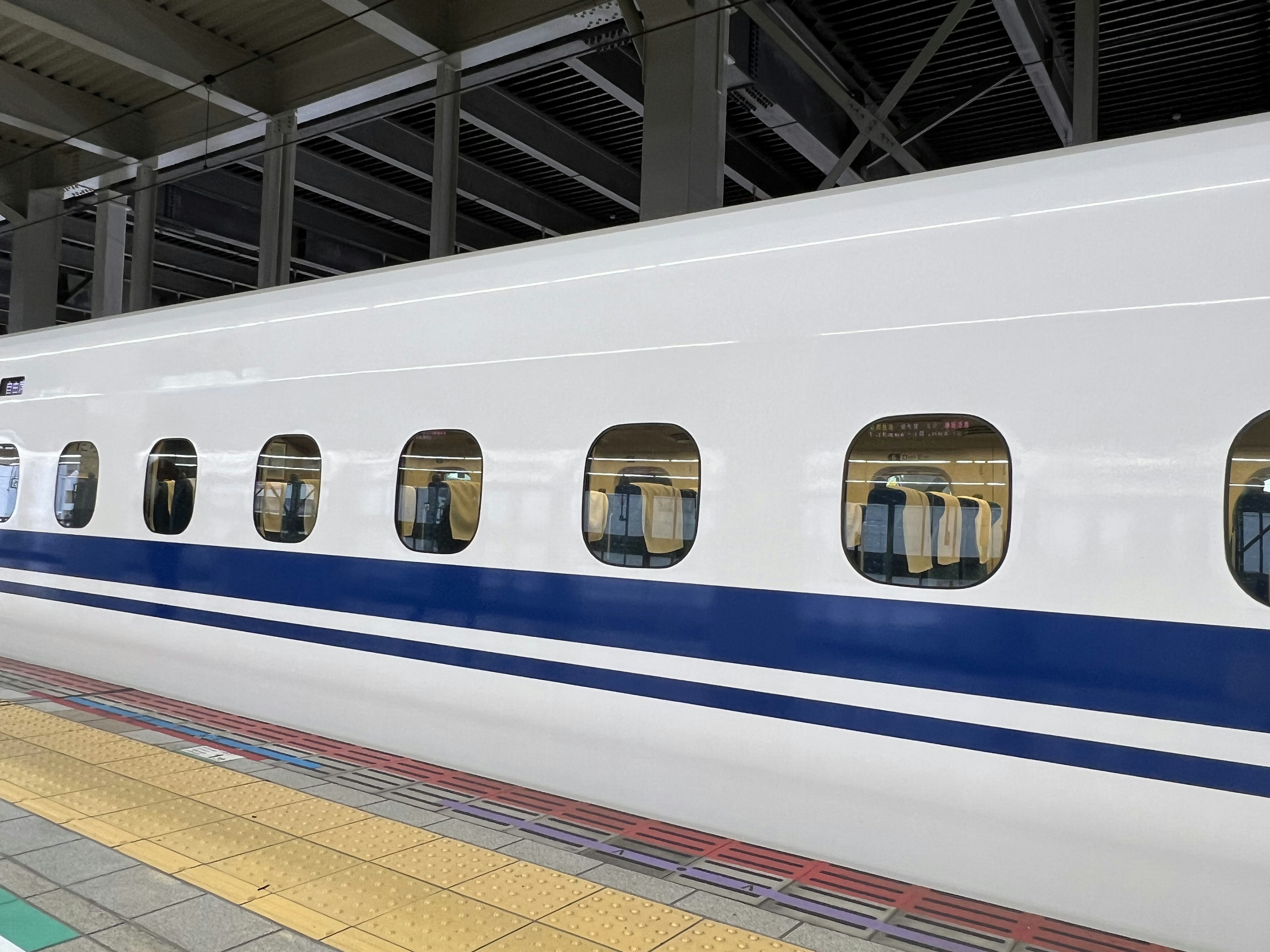 Side view of a Shinkansen train with white exterior and blue stripe windows