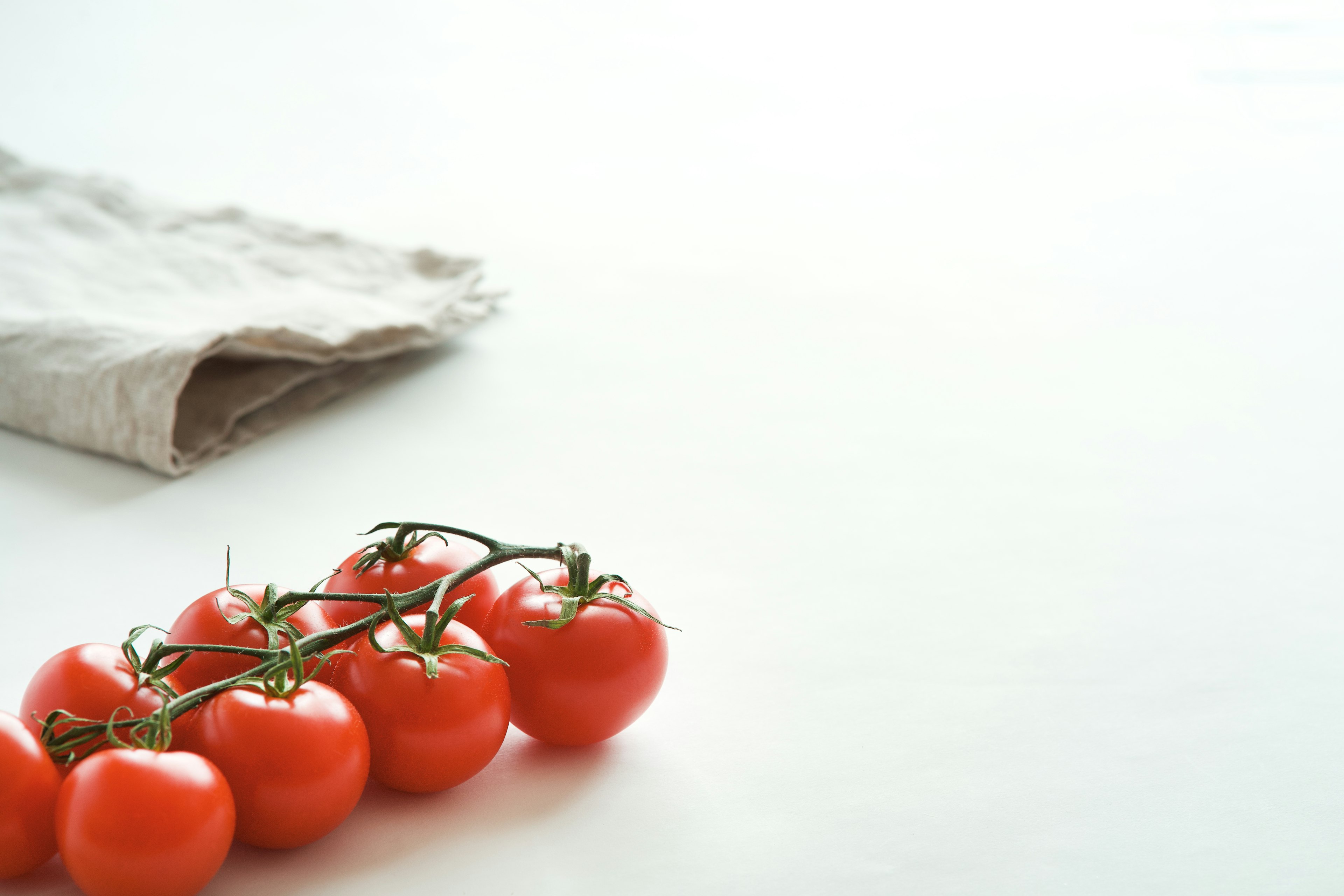 Fresh tomatoes on the vine next to a linen cloth on a simple table