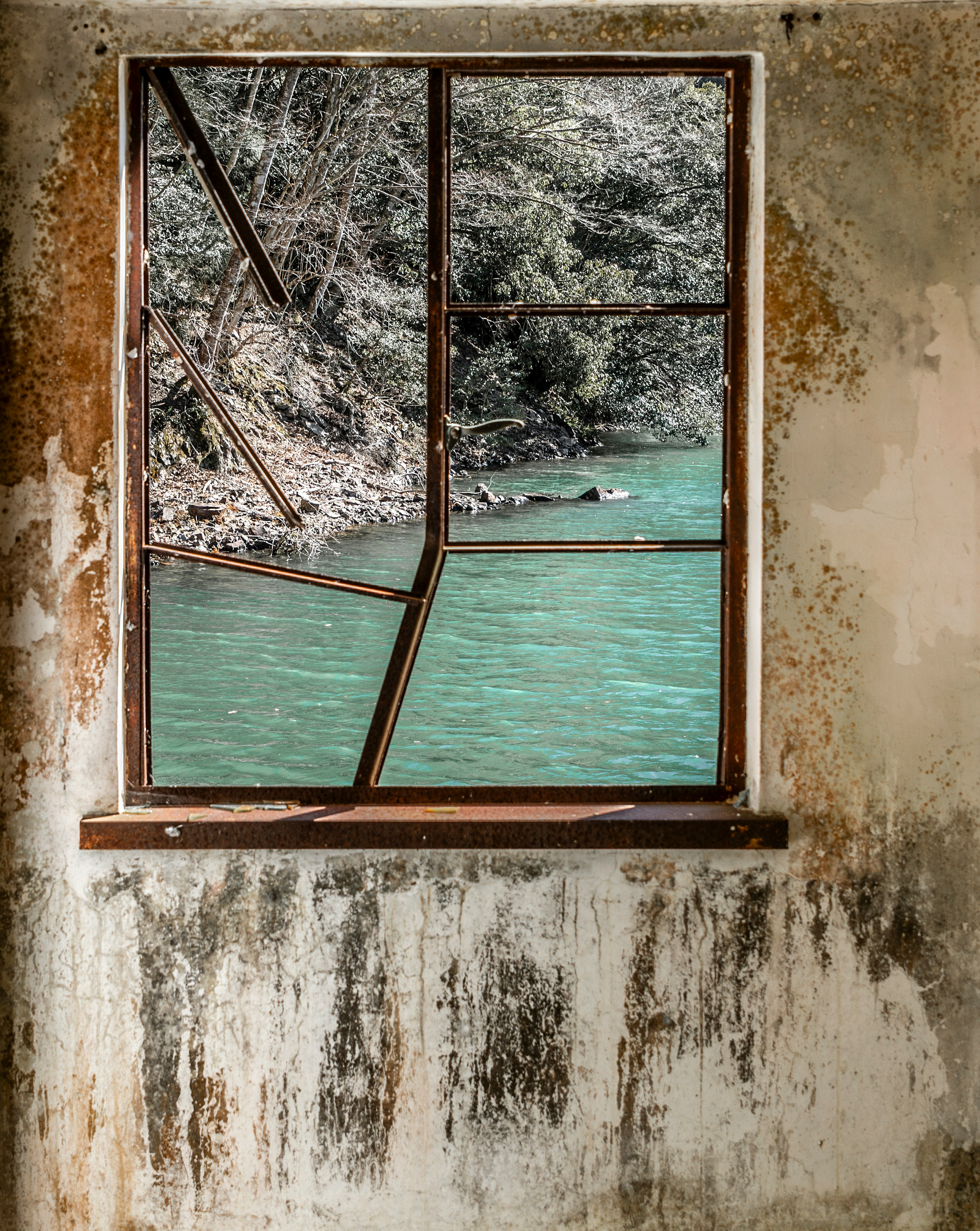 Alter Fensterrahmen mit Blick auf grünes Wasser und verwitterte Wand