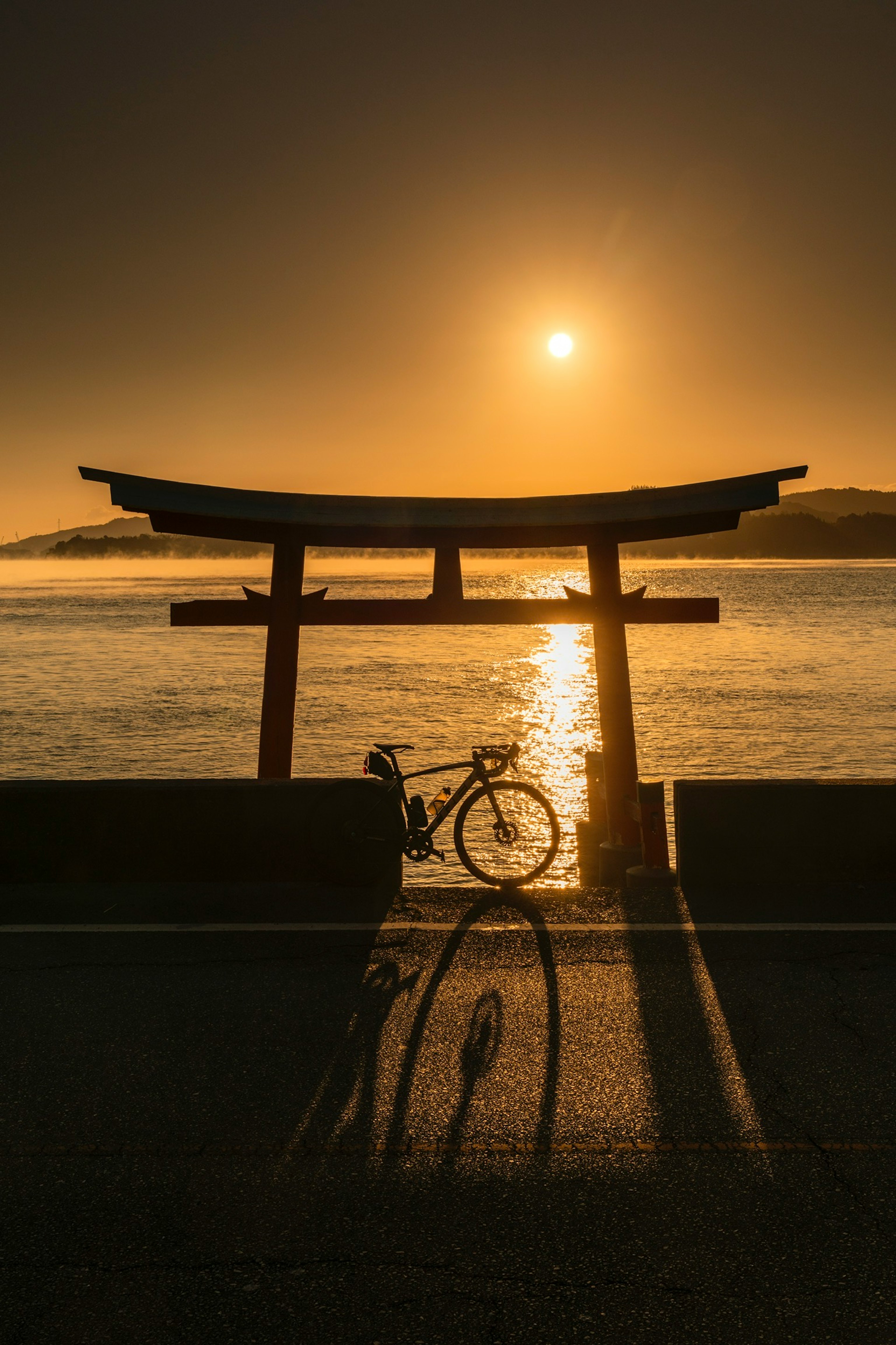 Puerta torii silueteada contra el atardecer con la sombra de una bicicleta