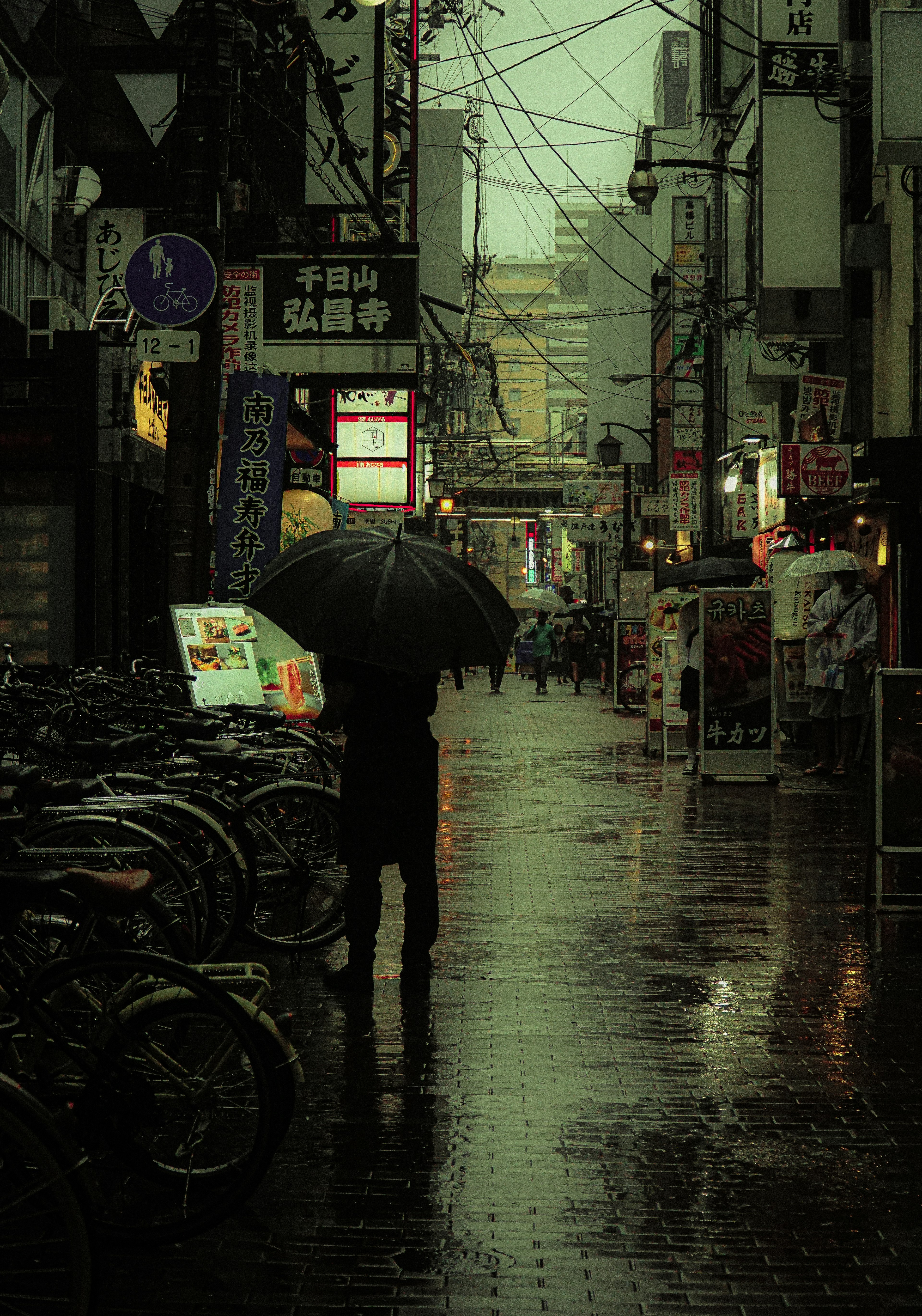 雨の中で傘をさした人が歩いている街の風景