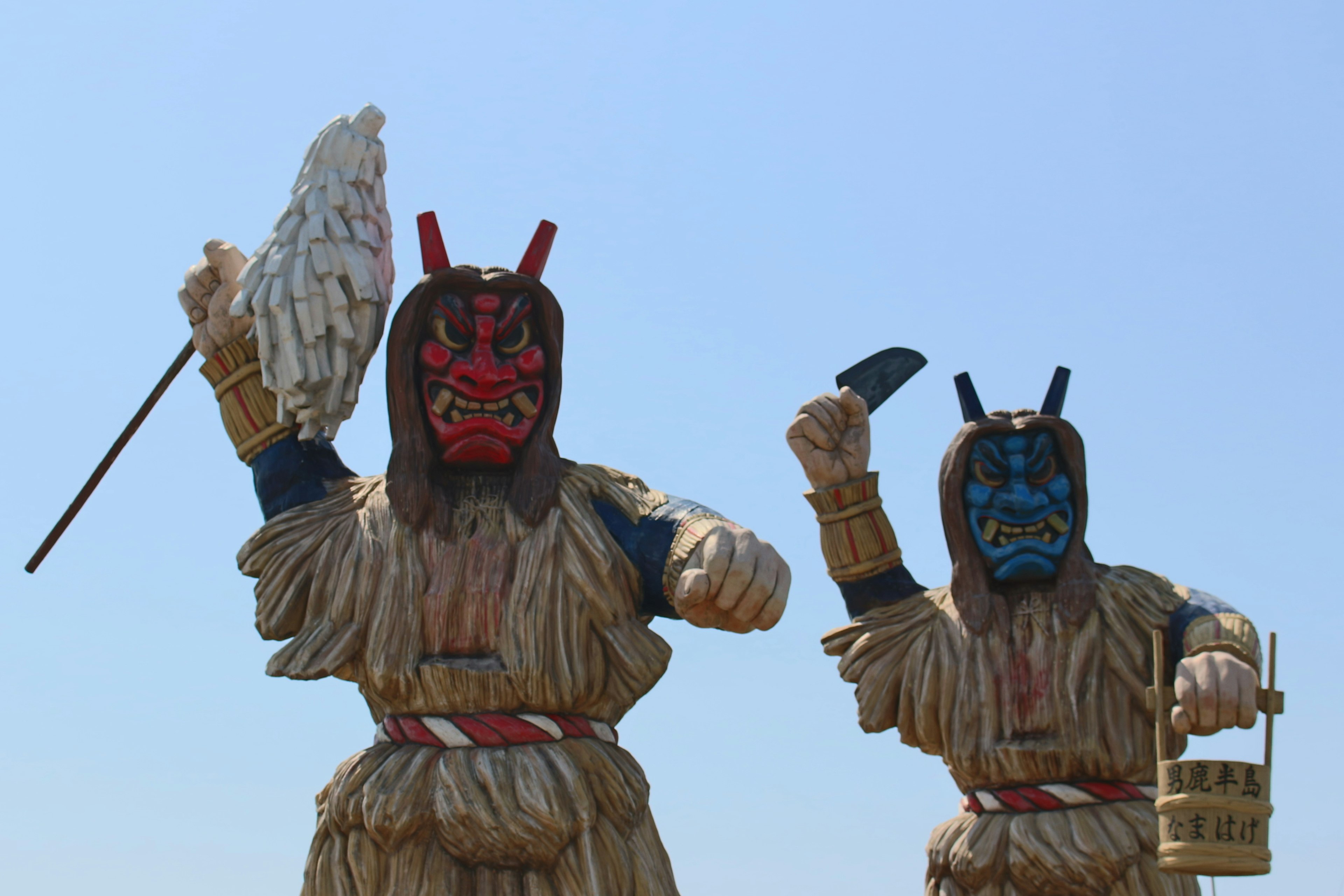 Two large demon statues with red and blue faces against a clear blue sky