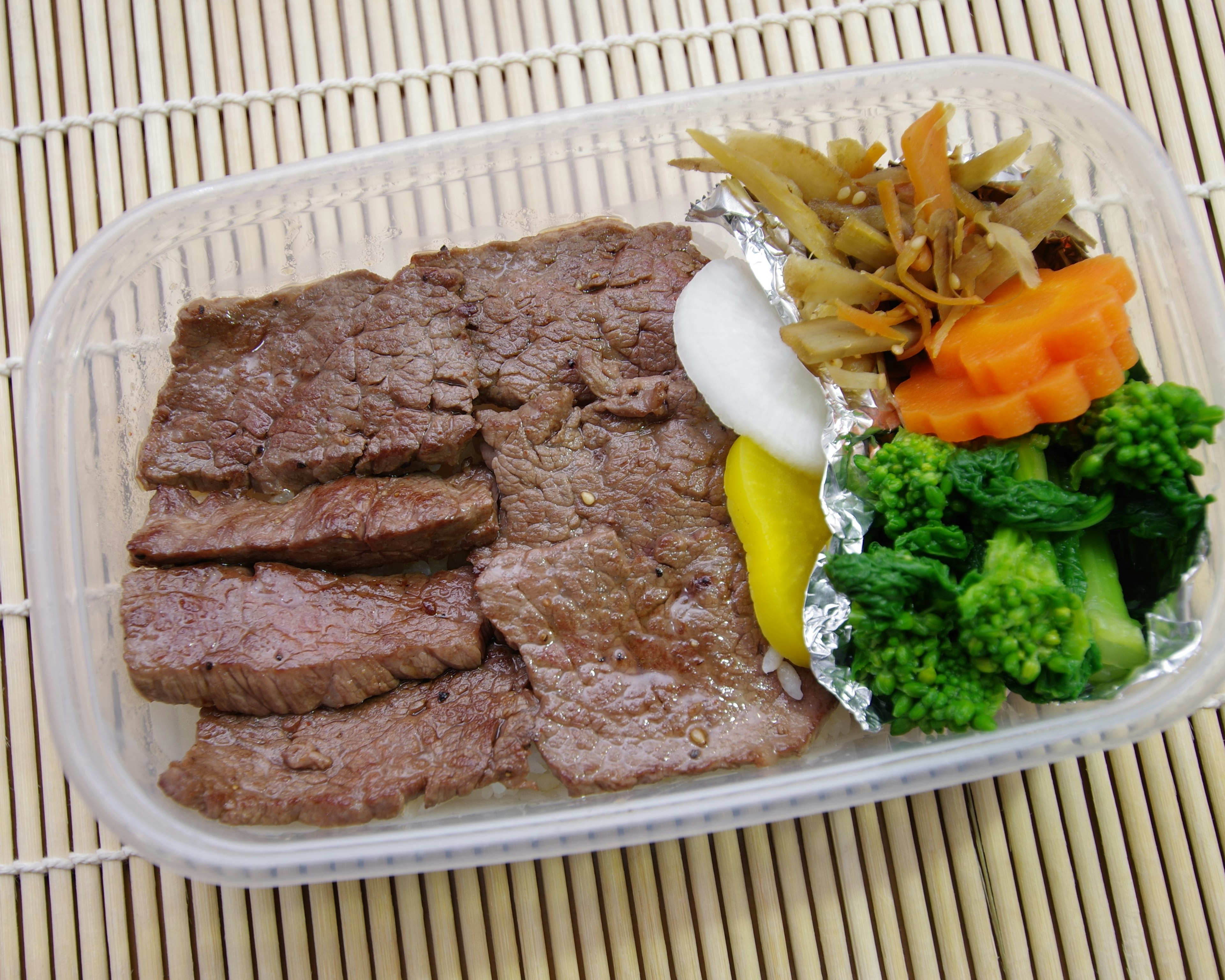 Carne de res en rodajas servida en una caja bento con verduras