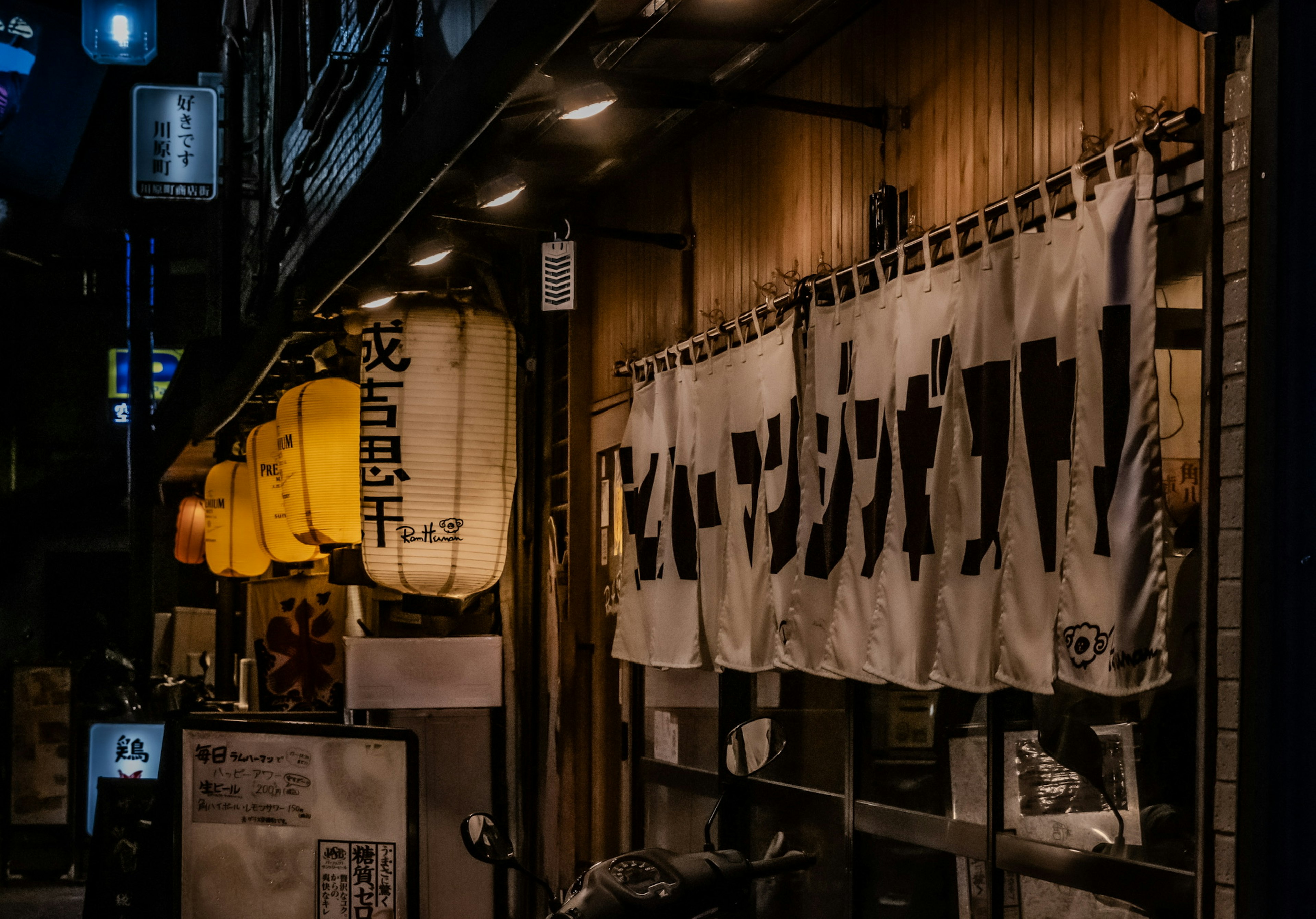 Extérieur d'un restaurant avec des lanternes jaunes et des rideaux noren traditionnels la nuit