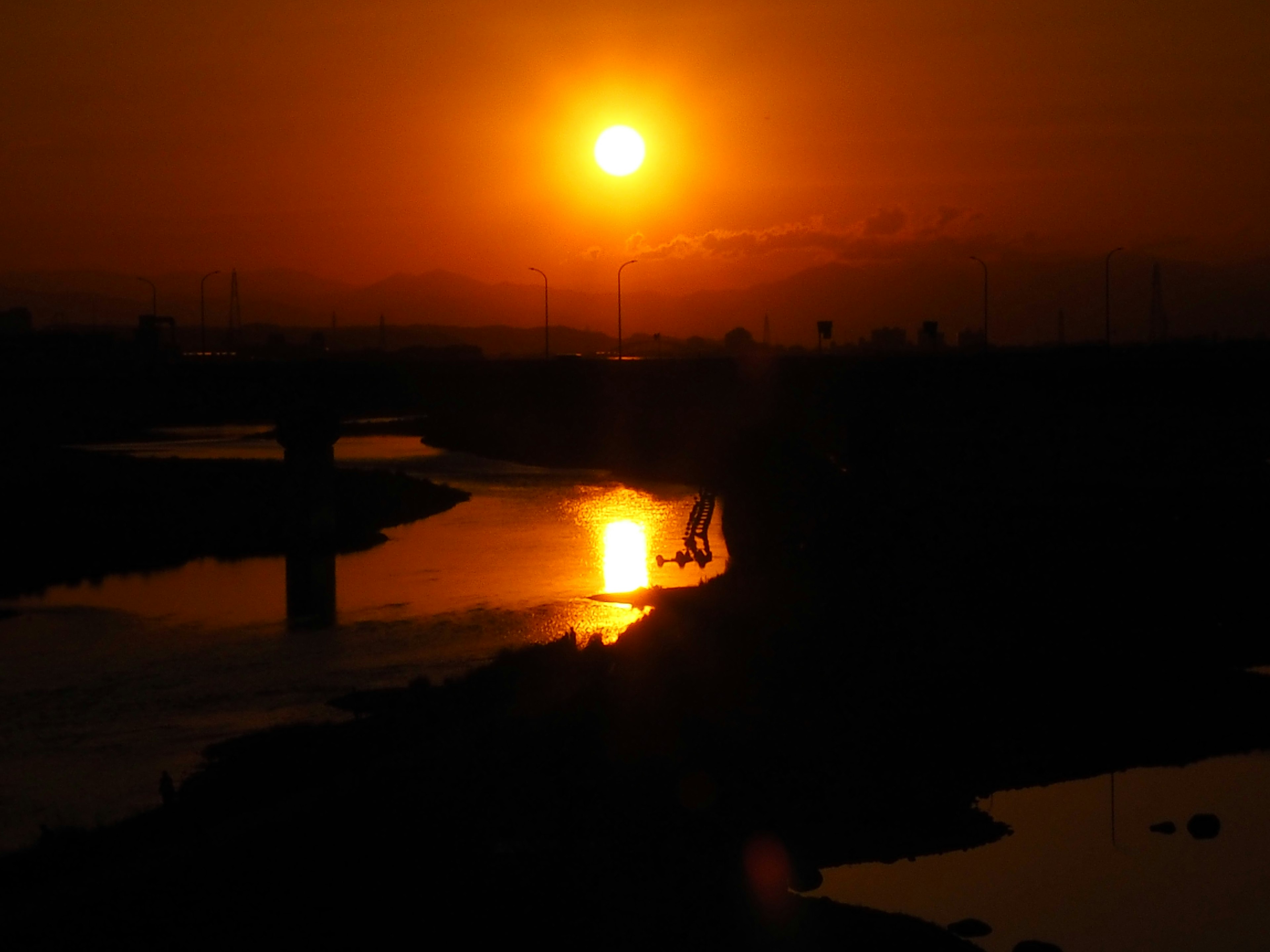 Atardecer sobre un río con reflejos en el agua cielo naranja y siluetas