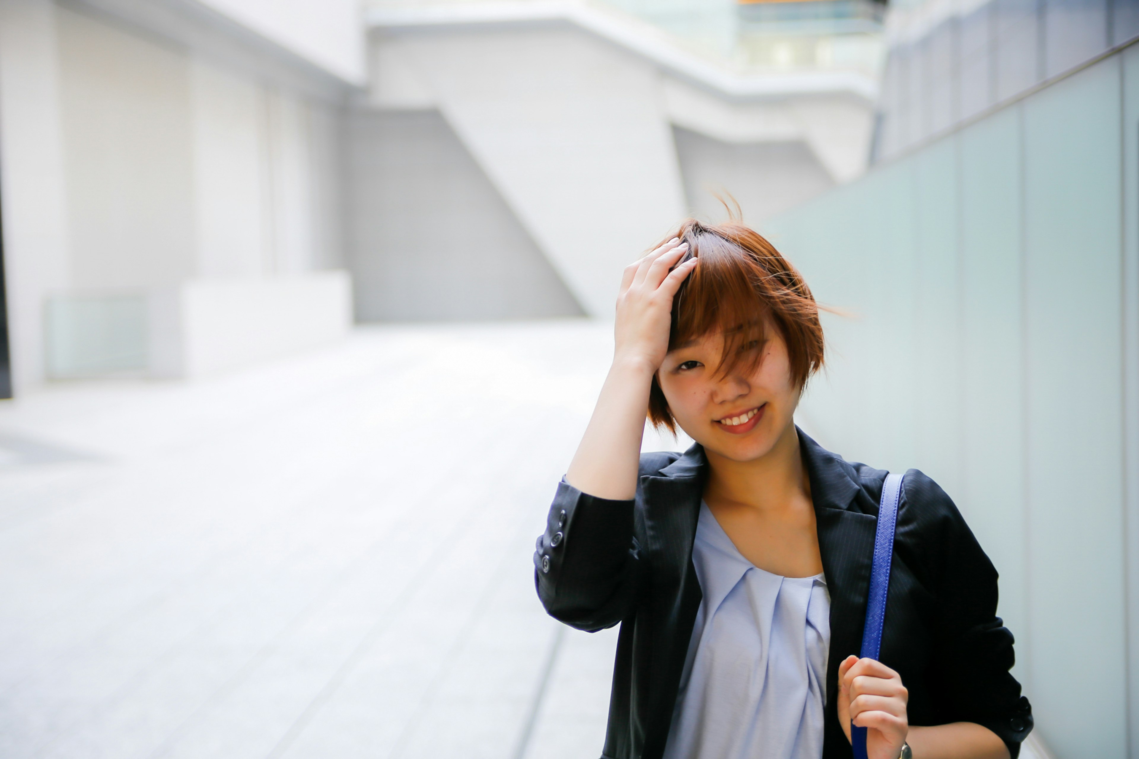 Une femme souriante ajustant ses cheveux dans un cadre urbain