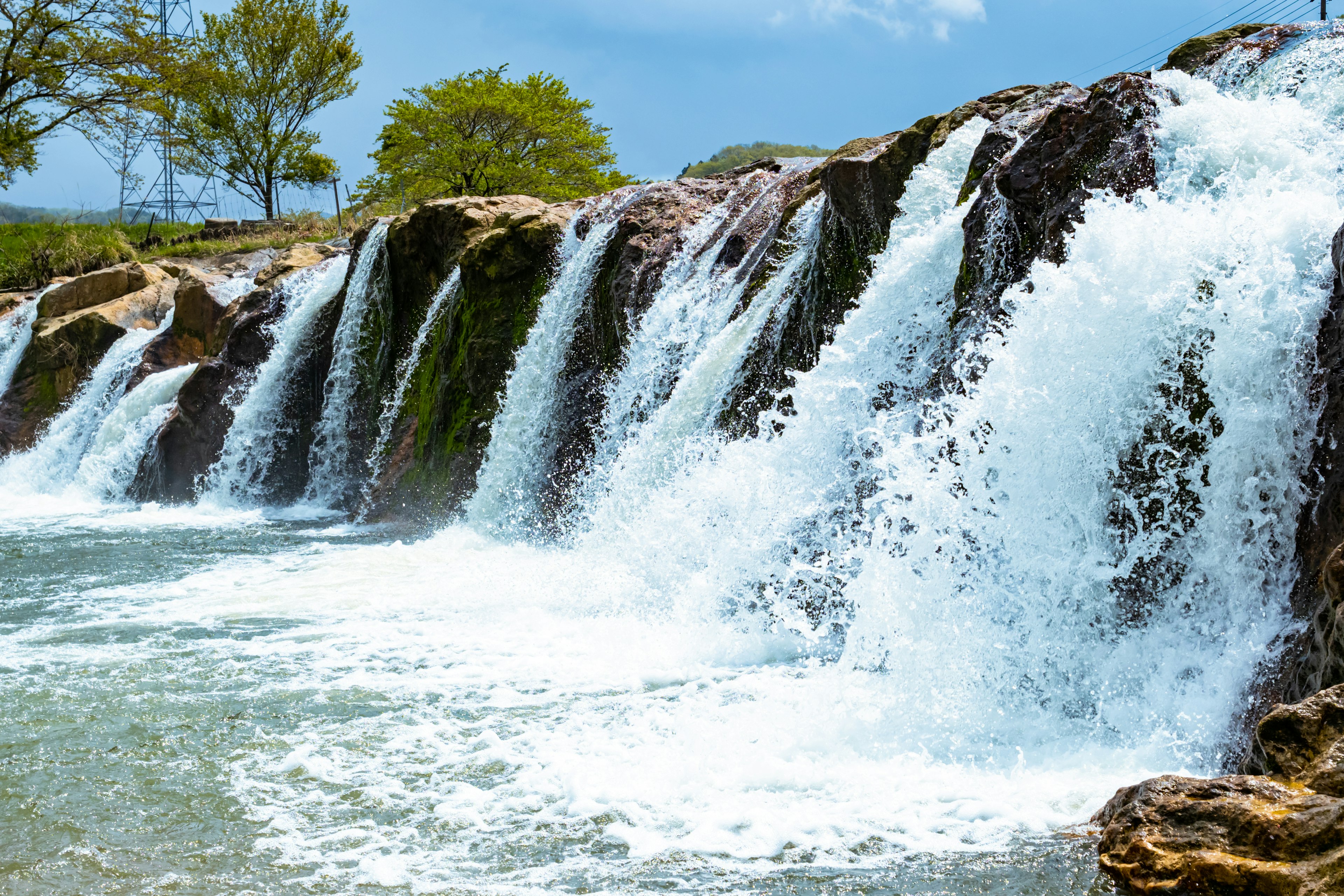 Bellissimo scenario di cascata spruzzi d'acqua cielo azzurro e alberi verdi