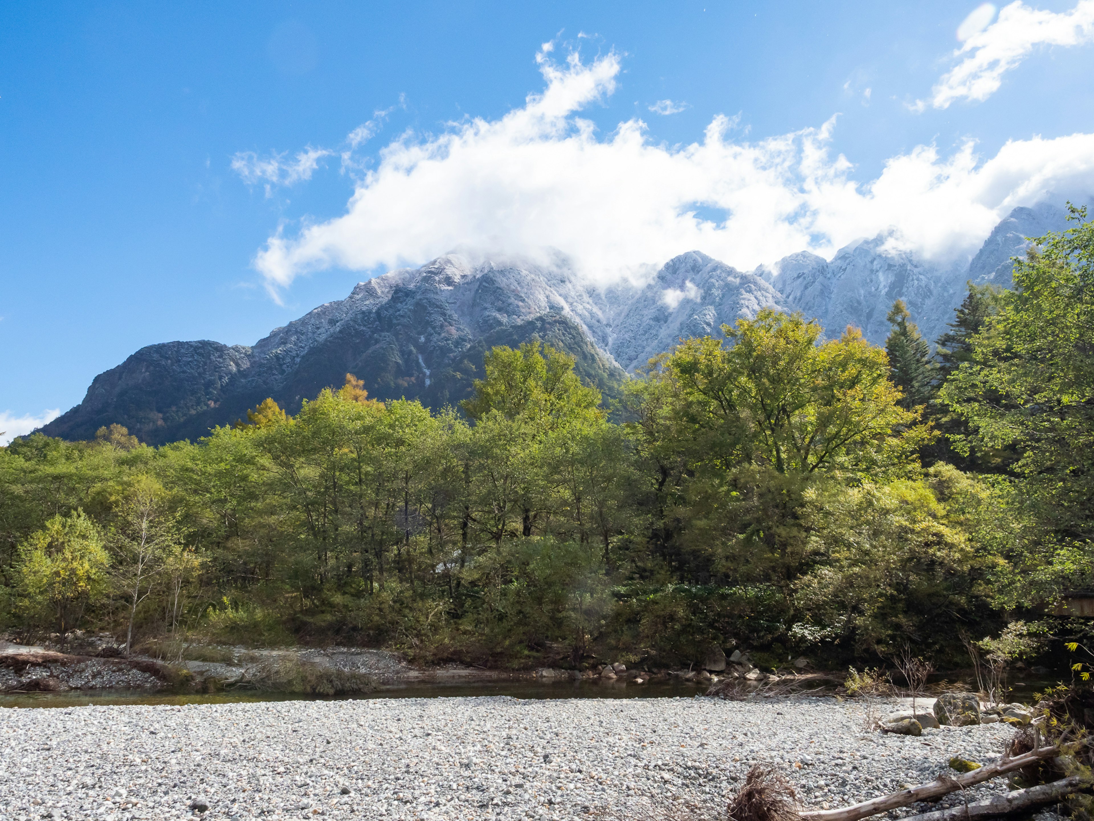 Malersicher Blick auf Berge mit Wolken und grünen Bäumen unter einem blauen Himmel