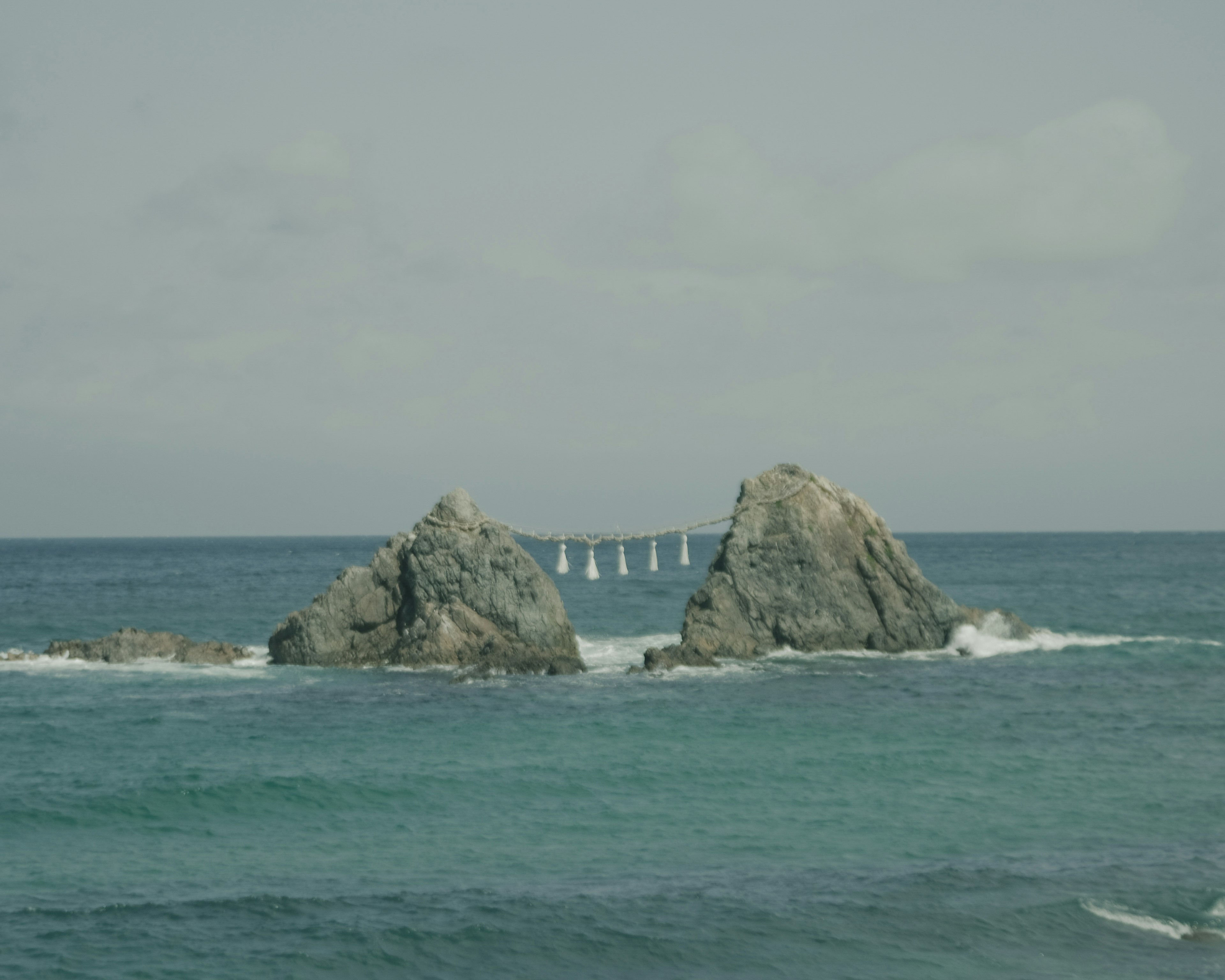 海の中にある二つの岩とその背後にかすかに見える橋