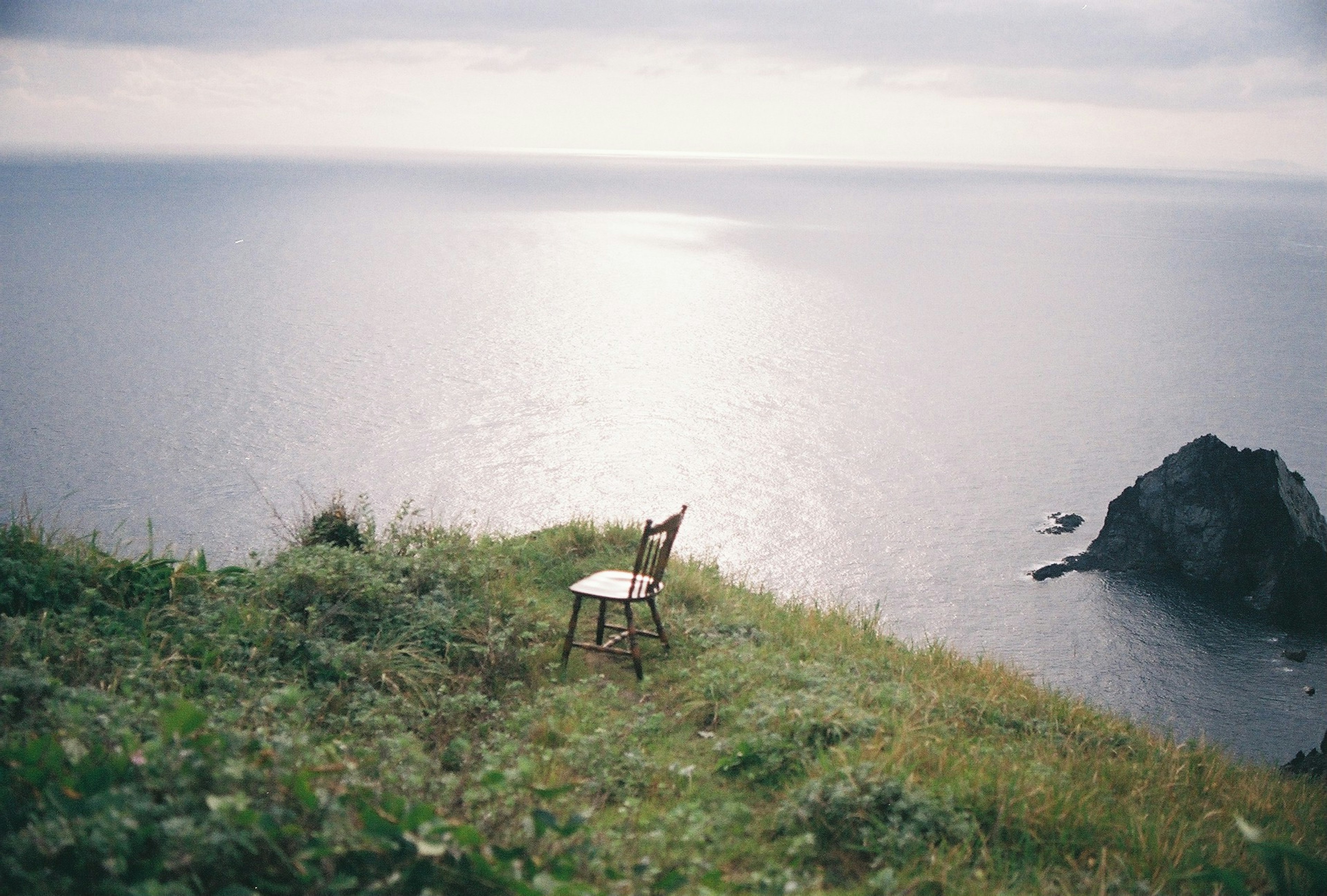 A chair placed on a grassy hill overlooking the ocean