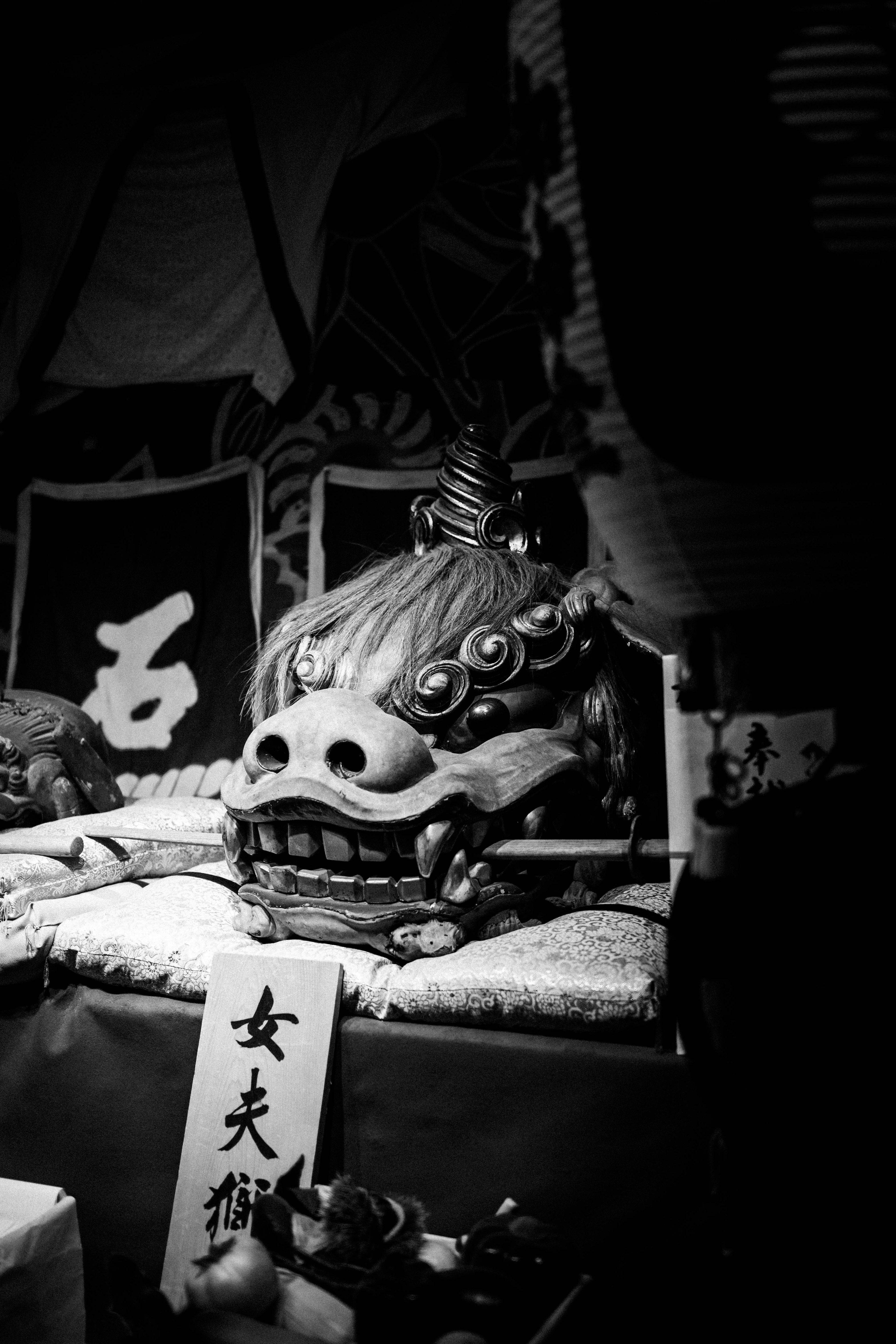 Schwarzweißbild einer traditionellen japanischen Löwentanzmaske, die bei einem Festival ausgestellt ist