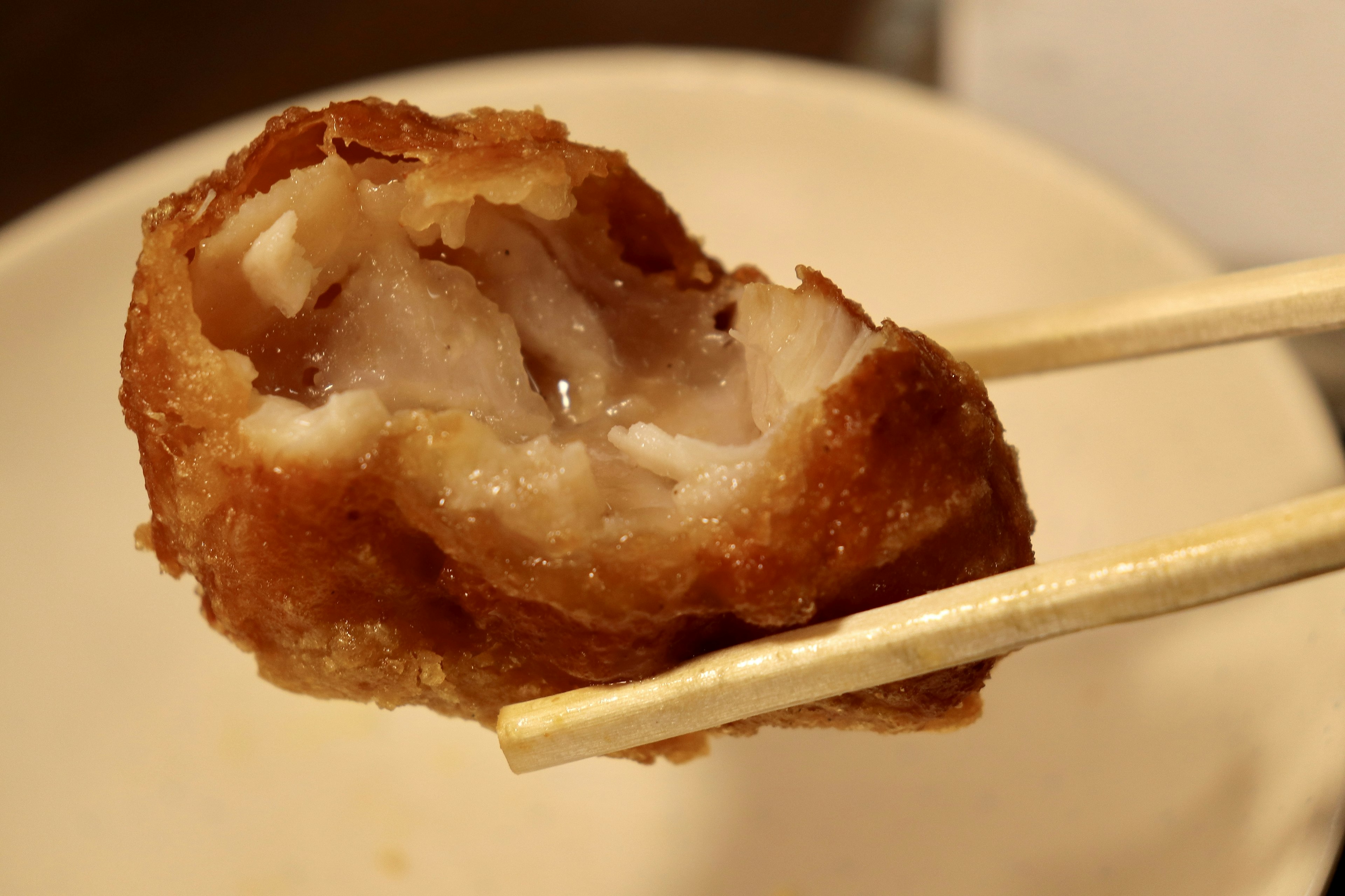 A piece of fried chicken being held with chopsticks