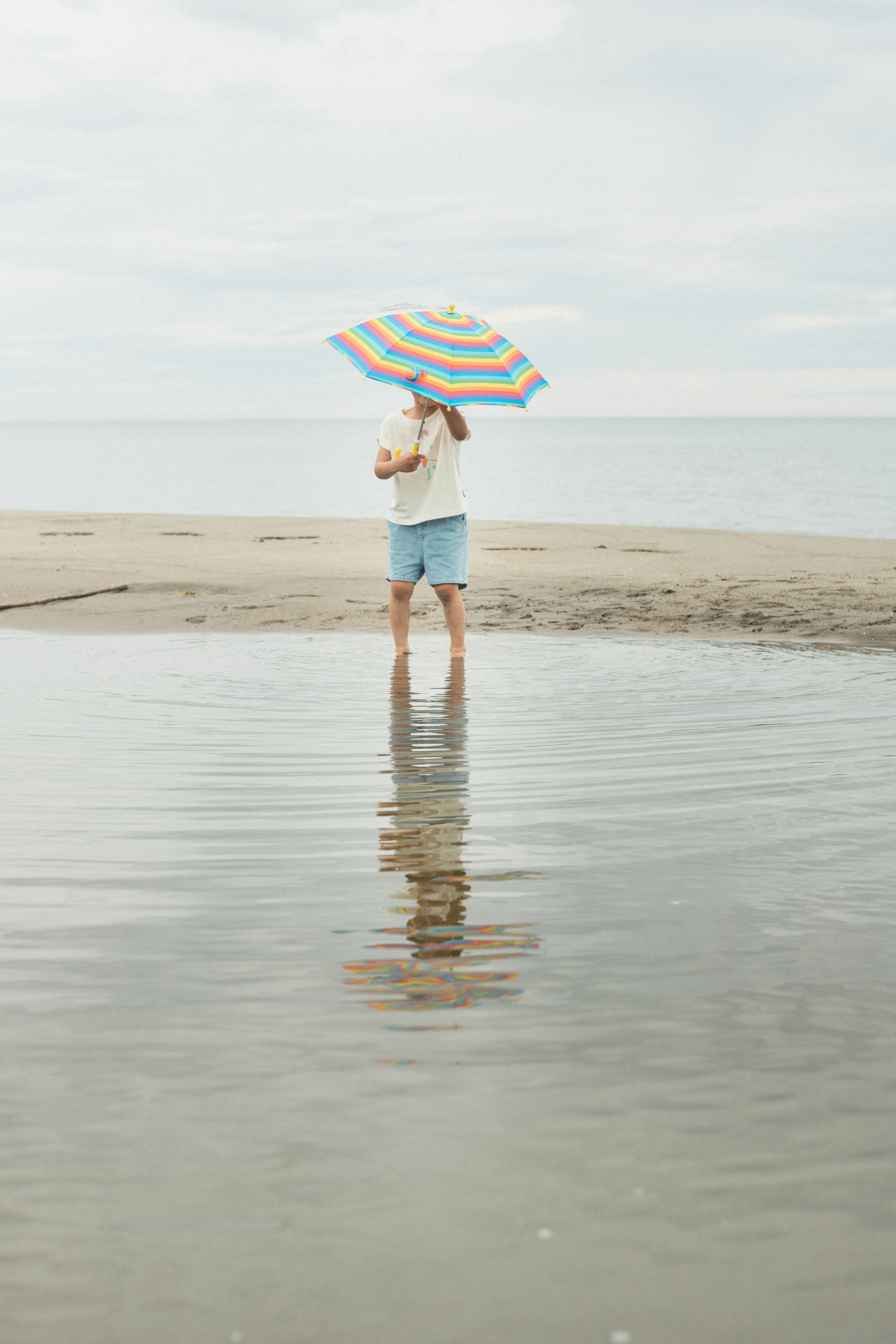 Mujer de pie en la playa sosteniendo un paraguas a rayas Reflejo en el agua Ambiente tranquilo