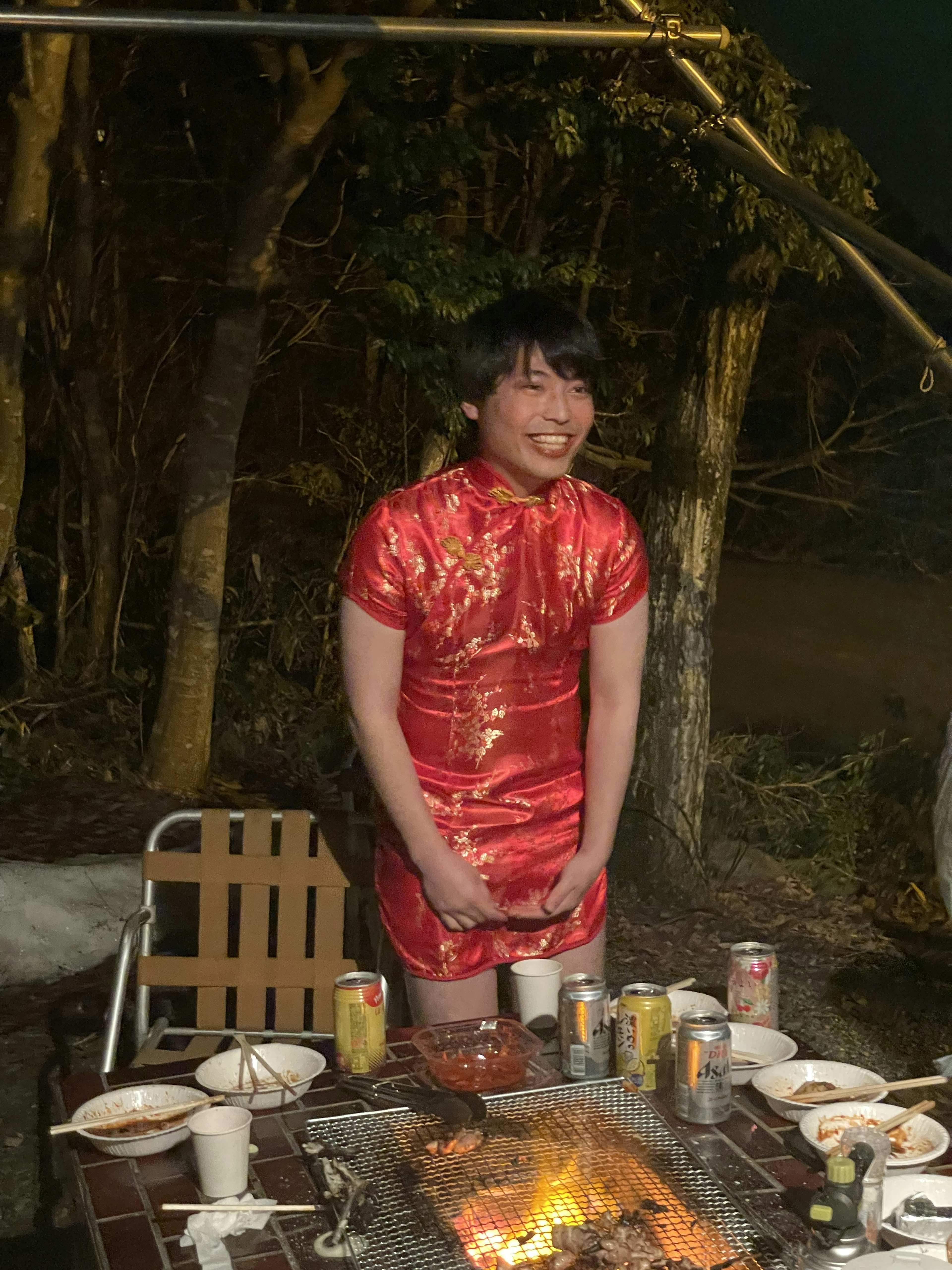 Un hombre con un cheongsam rojo está de pie frente a una mesa de barbacoa al aire libre