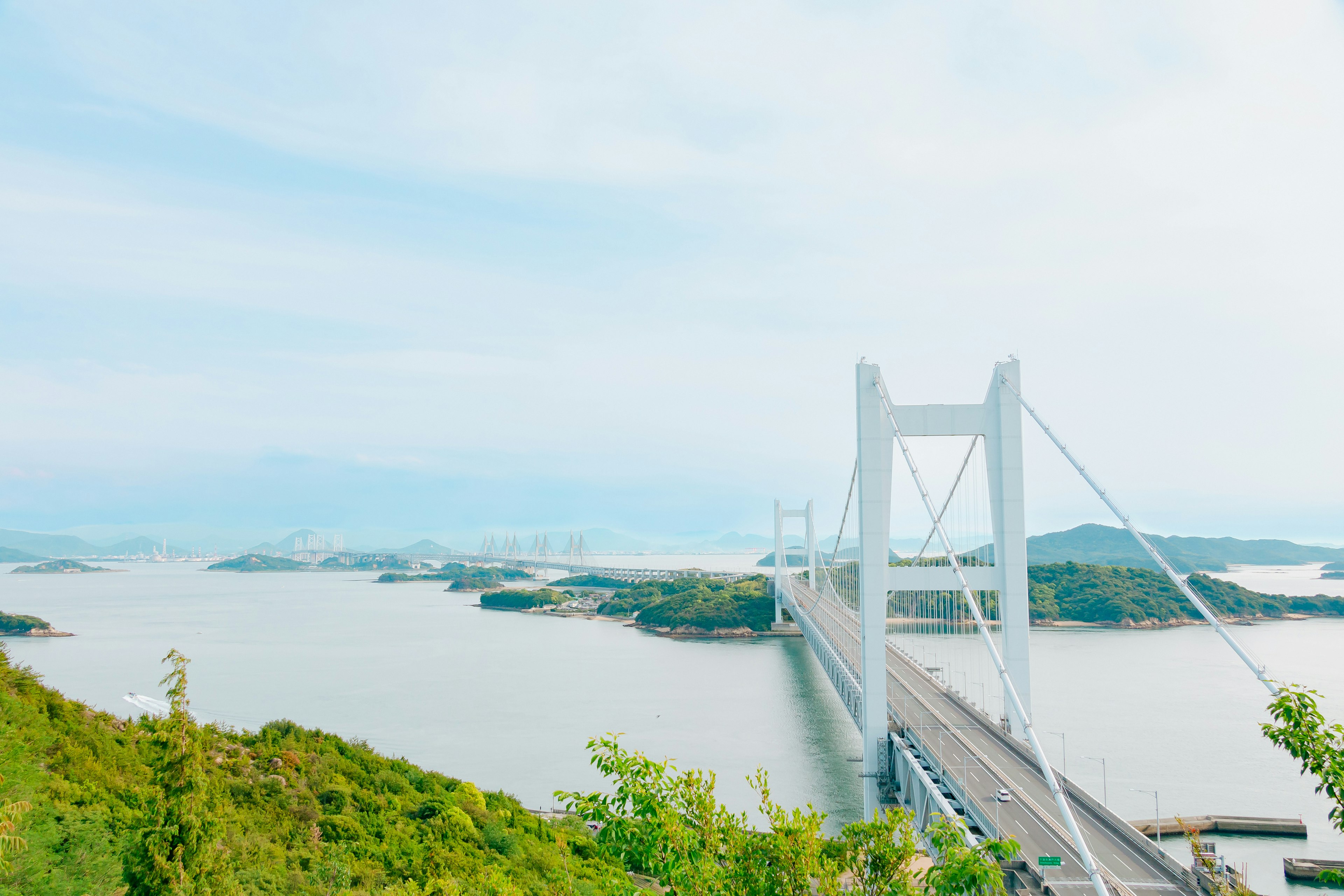 A scenic view of a white suspension bridge over calm blue waters and green hills