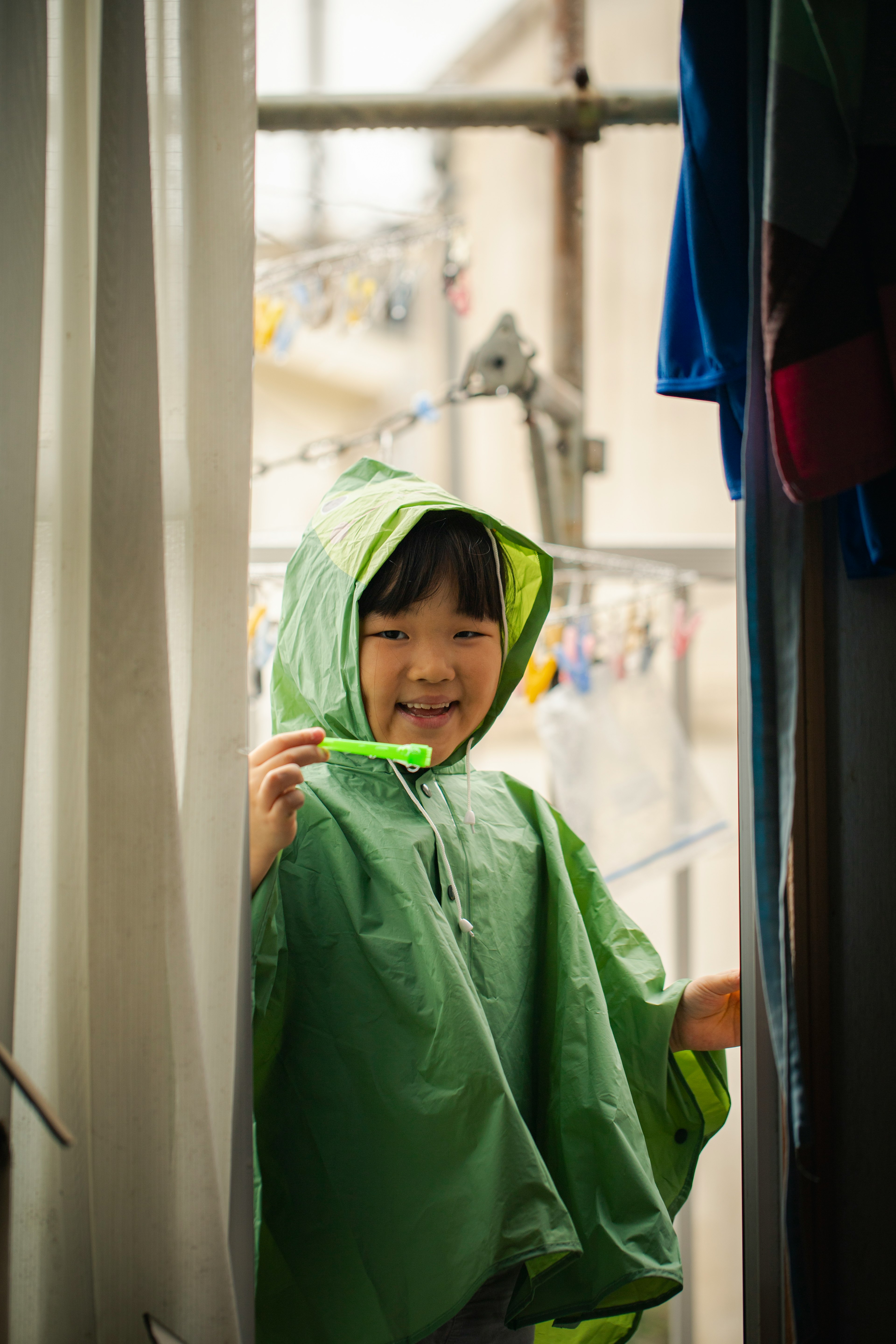 Niño sonriendo con un impermeable verde desde una puerta