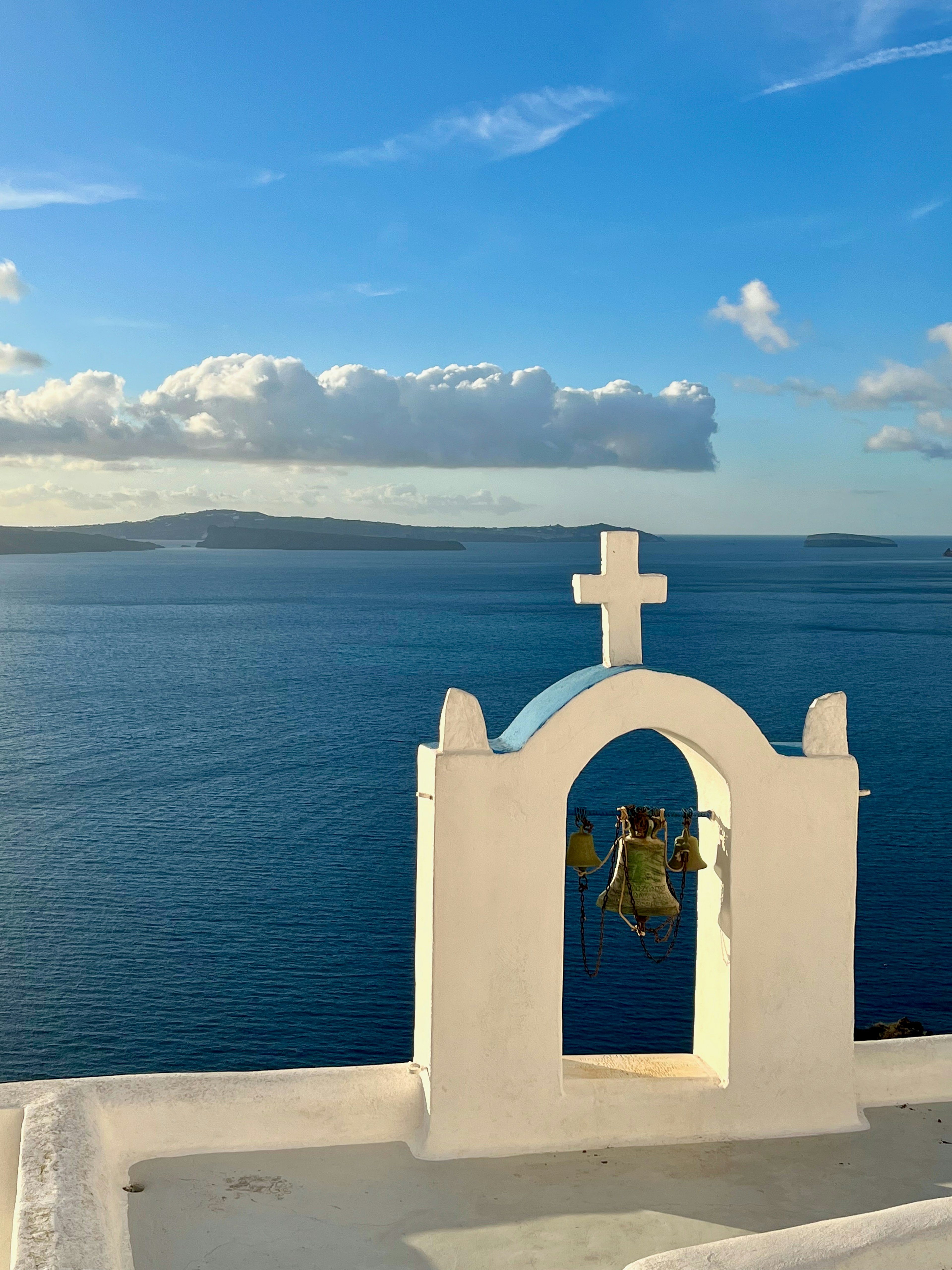 White church bell tower with a cross overlooking the blue sea and sky