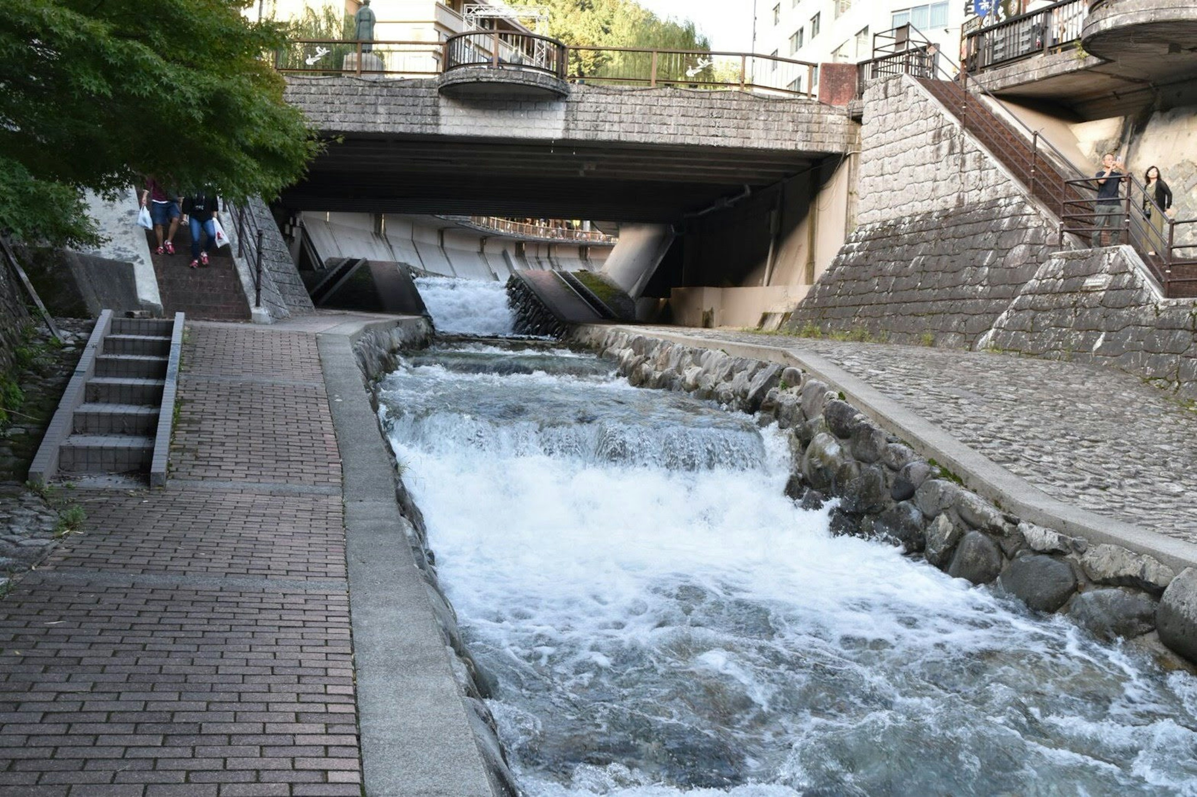 Ein fließender Fluss mit Steinböschungen und einem Fußweg