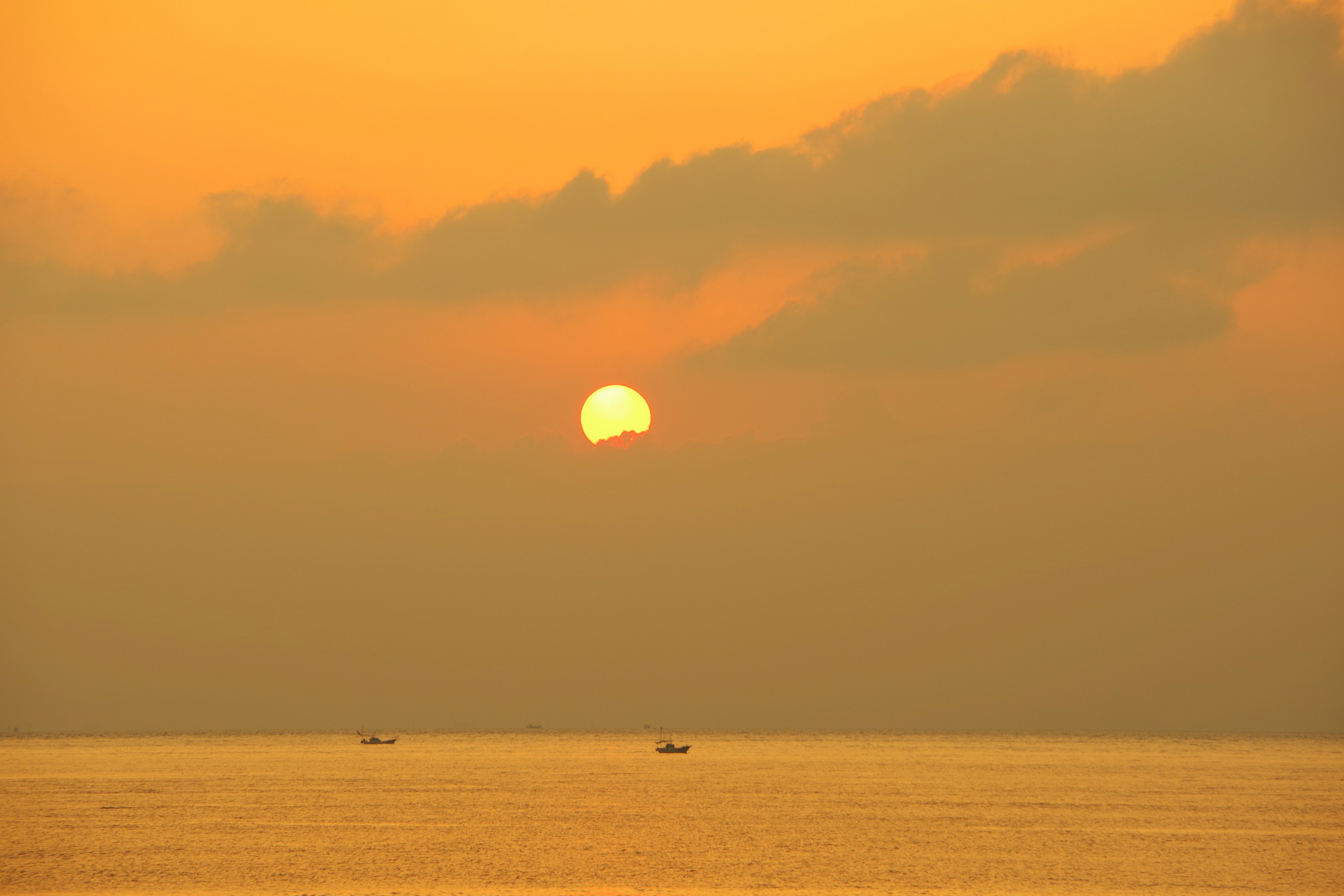 Sun setting over the ocean with boats in the distance