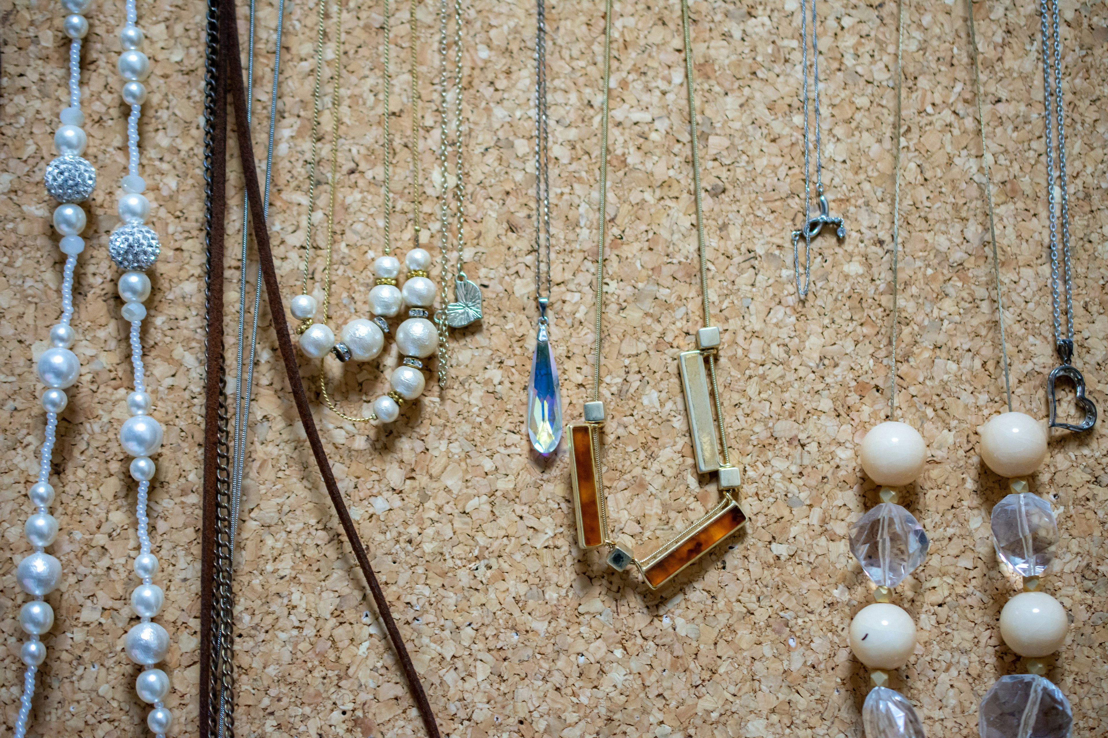 A collection of necklaces displayed on a wall featuring pearls, metal, and glass elements