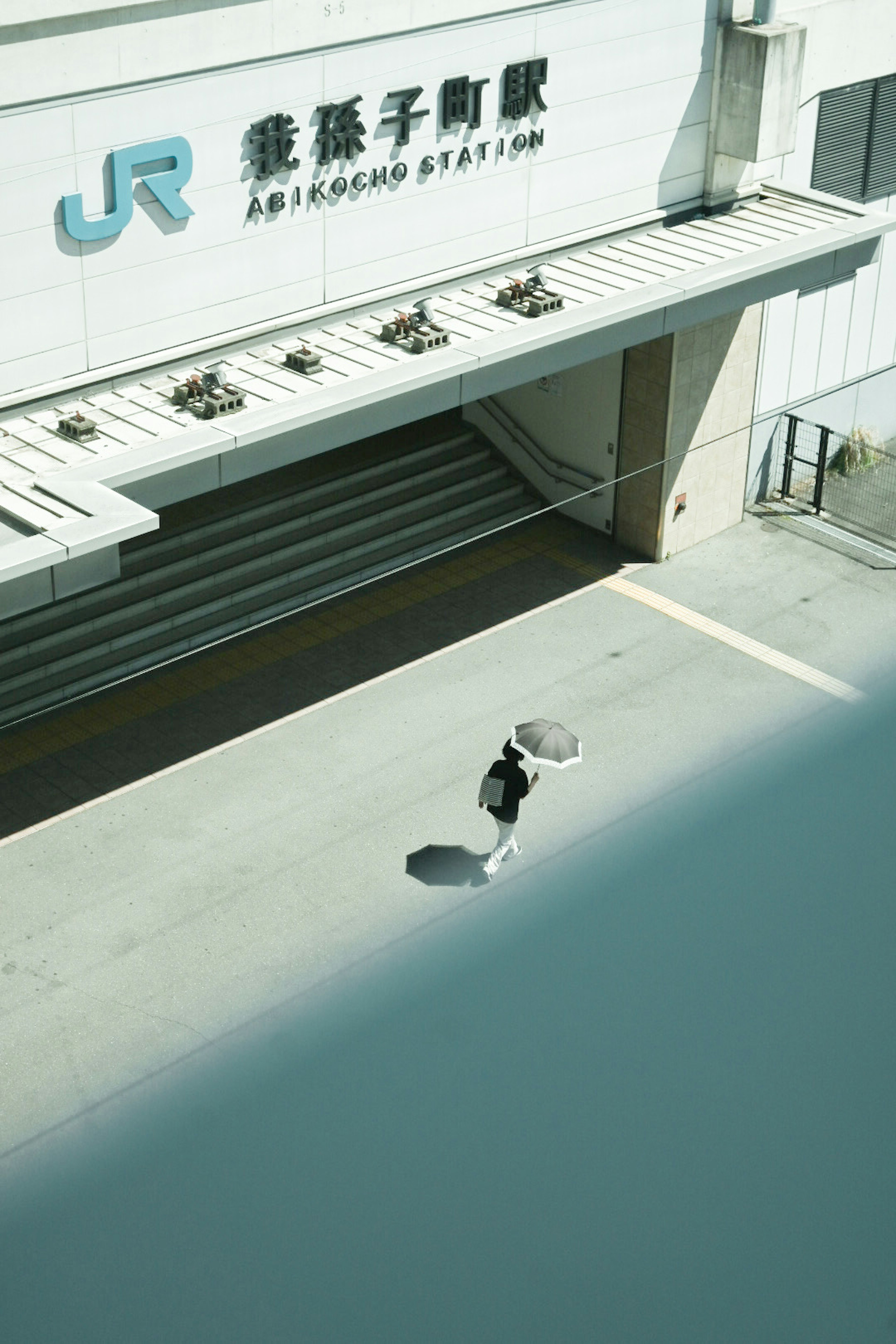 Exterior of a train station with a person holding an umbrella walking