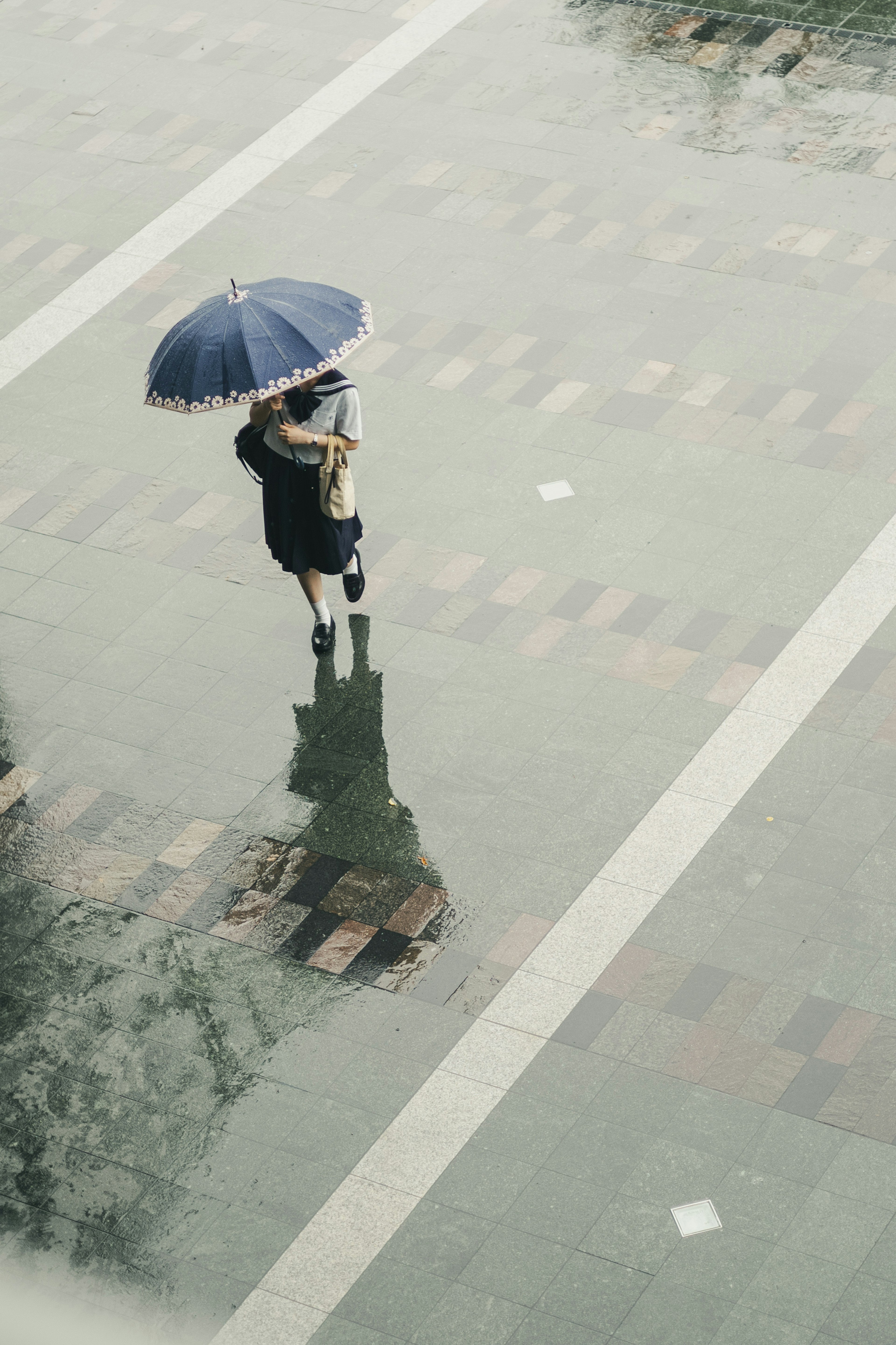 Una persona che cammina con un ombrello blu in un giorno di pioggia con riflessi sul pavimento