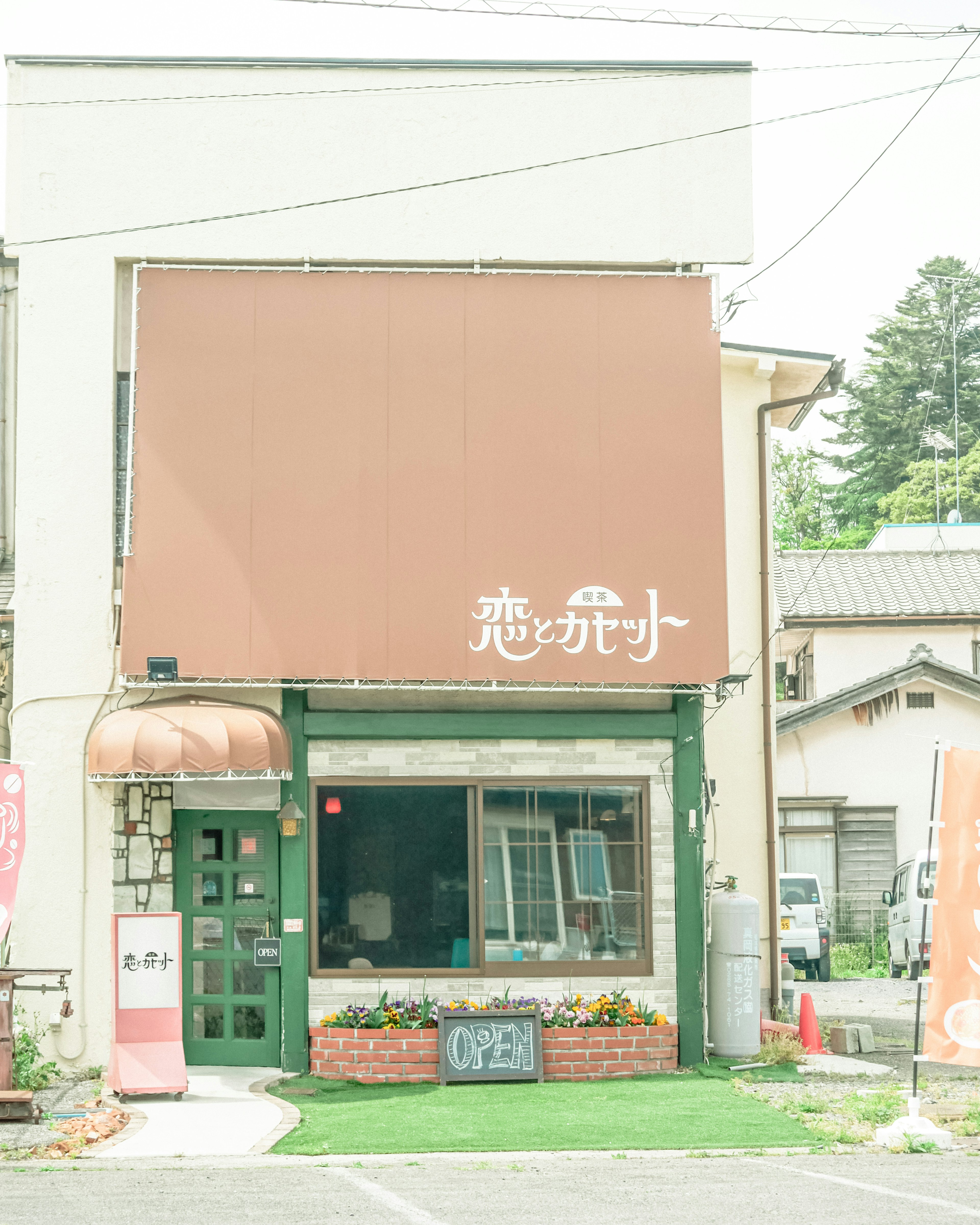 Facade of a small cafe with a brown canopy green walls and large windows