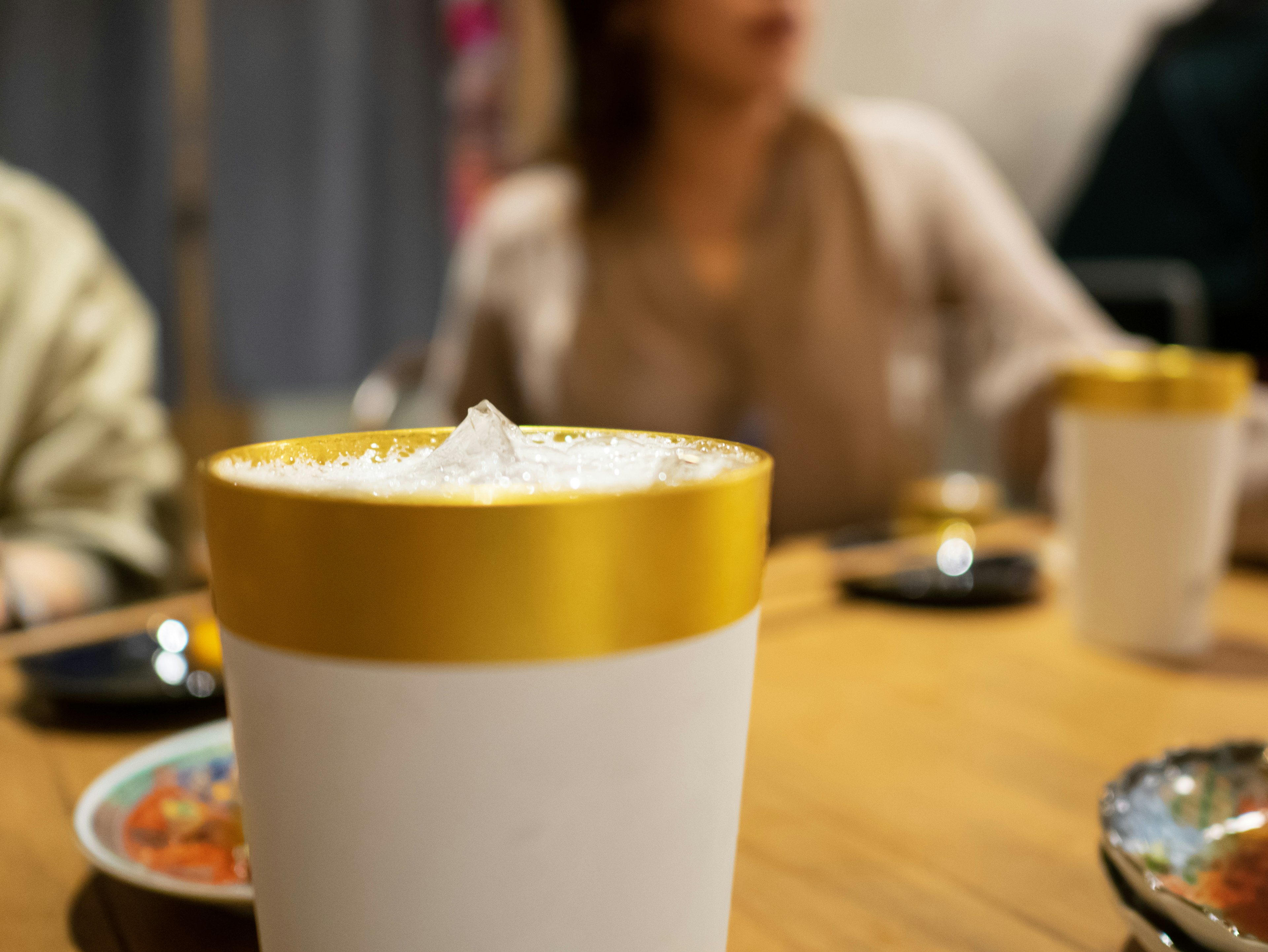 A drink with a gold lid on a table with blurred people in the background