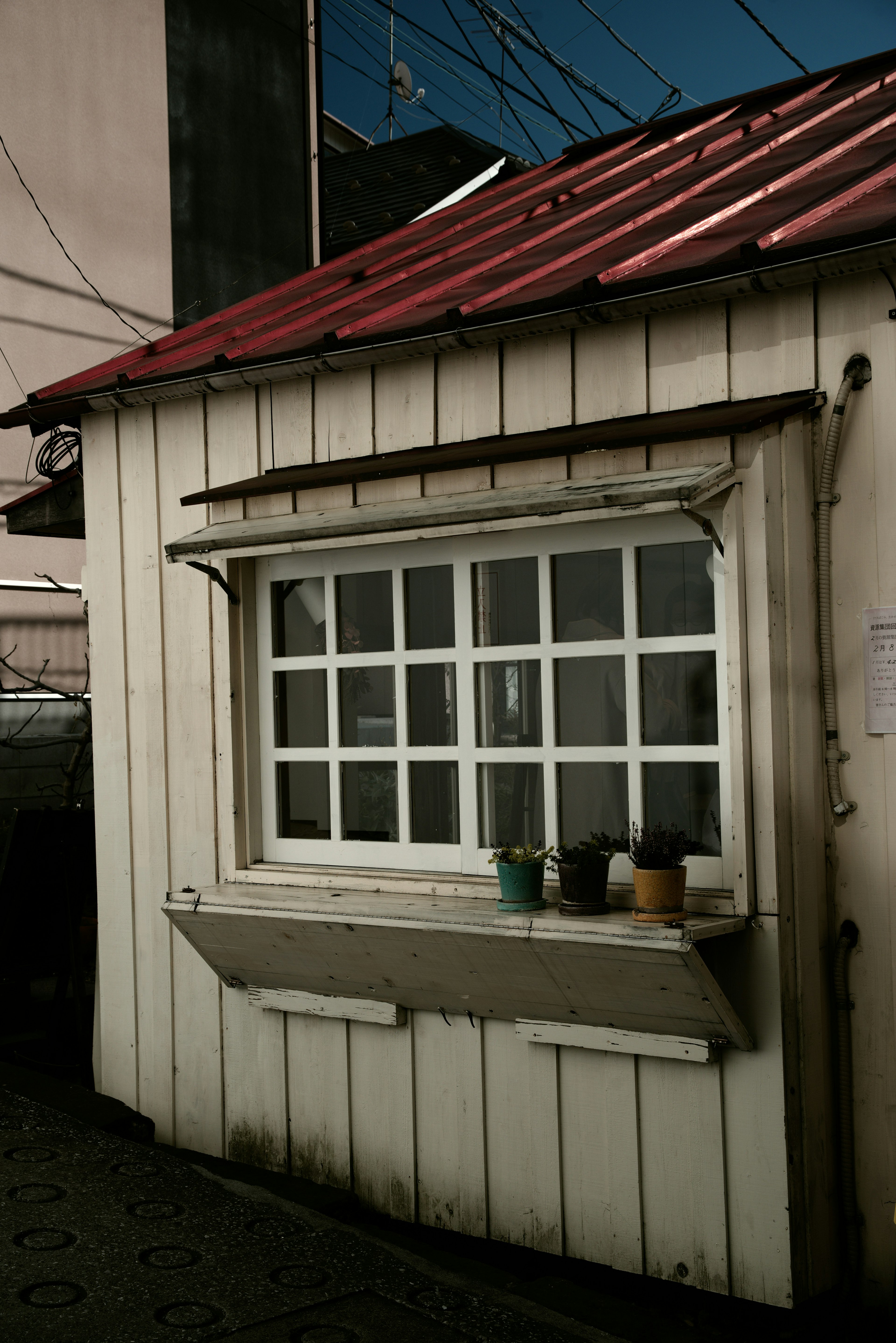 Petite cabane avec un extérieur en bois blanc et un toit rouge avec une fenêtre