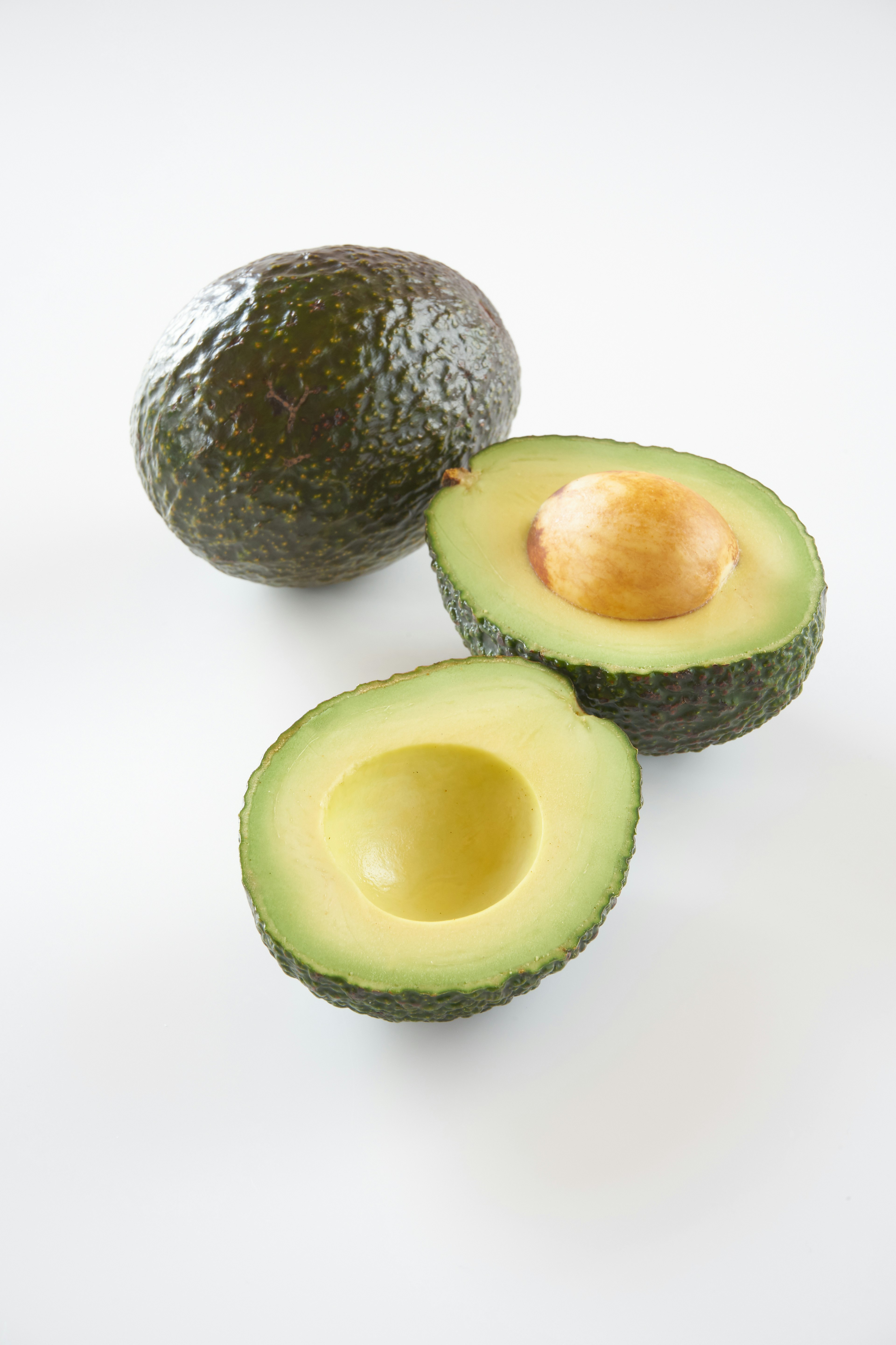 Bild von einer ganzen Avocado und einer halbierten Avocado mit sichtbarem Kern