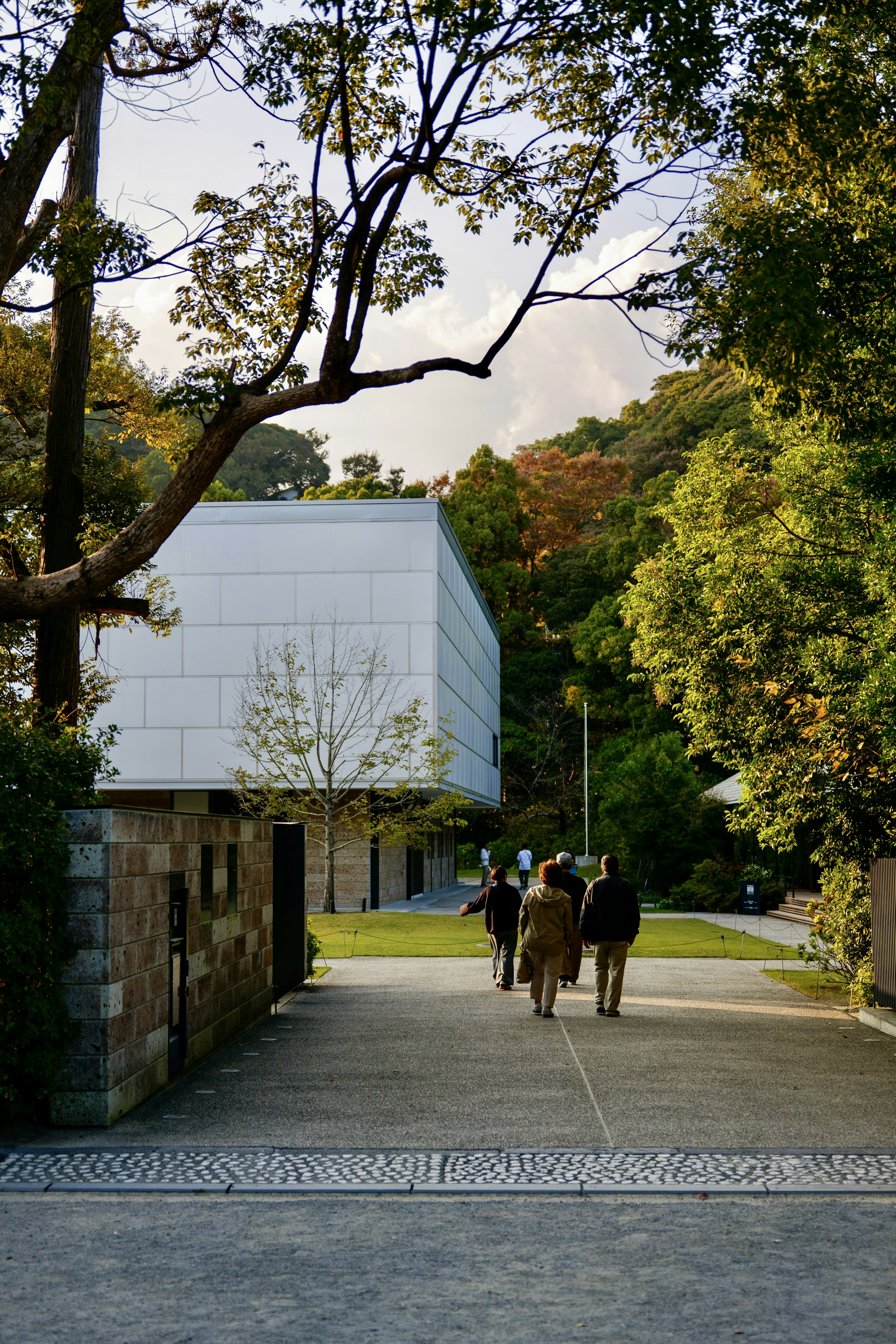 People walking on a quiet pathway with a white building and lush greenery